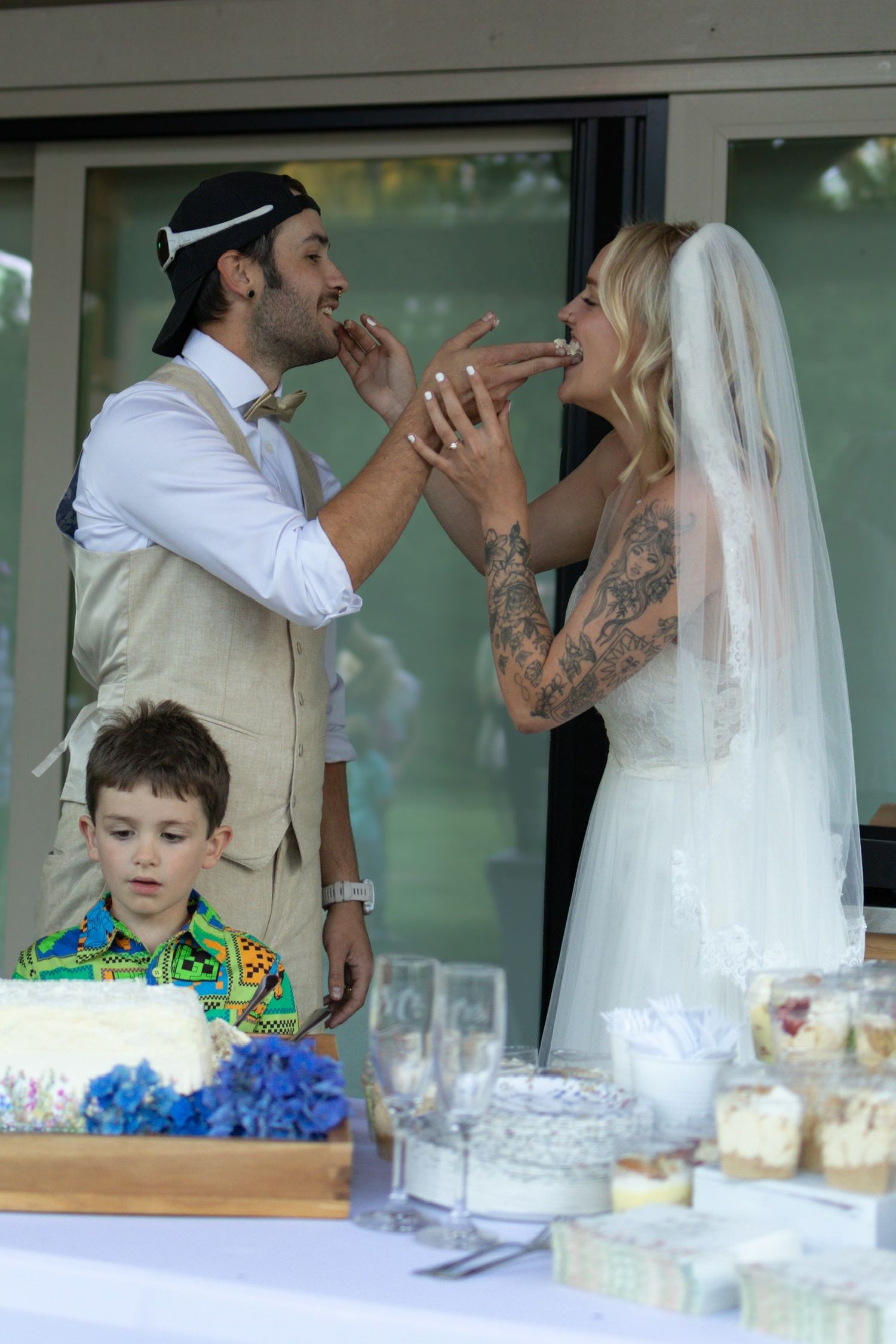 A joyful scene at a wedding reception with a bride in white and guests sharing laughter around the dessert table.