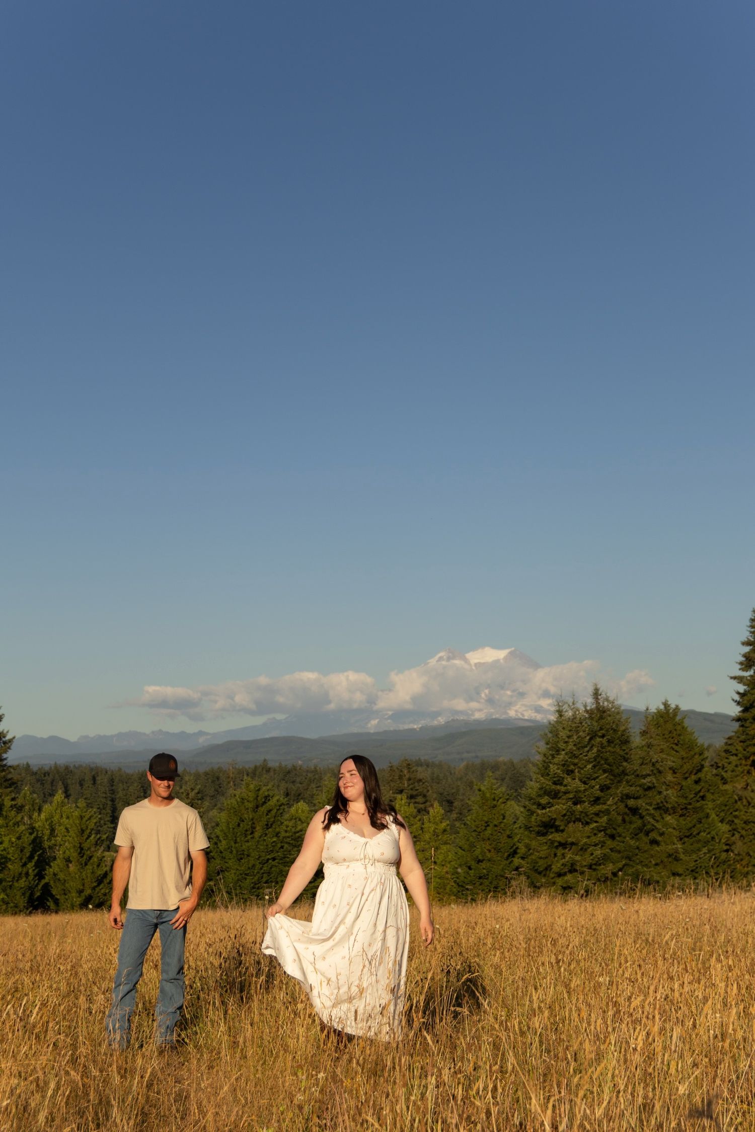 Couple in meadow with mountain range and evergreen forest backdrop.