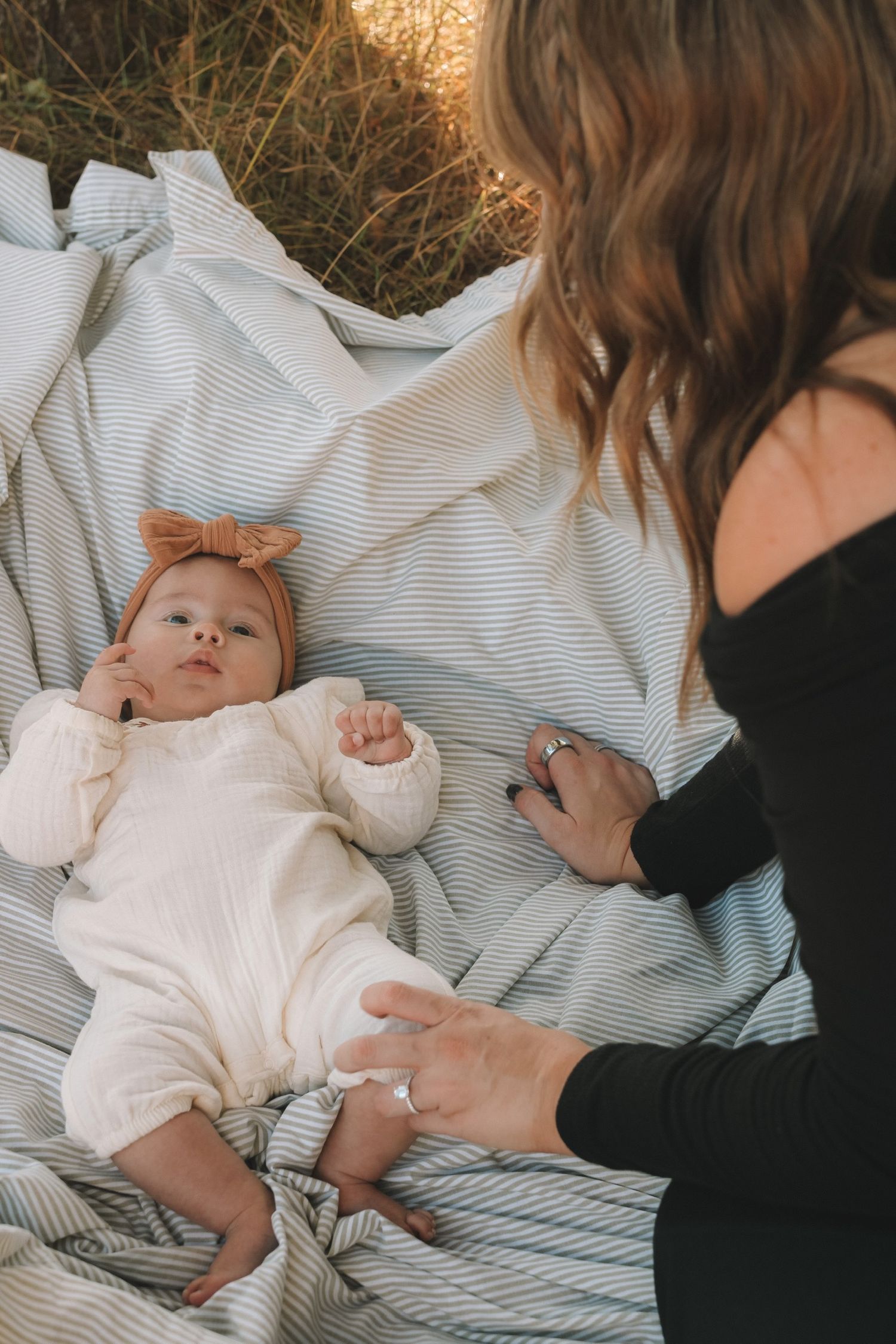 A series of candid moments showing a baby in white clothing lying on striped bedding while being comforted.