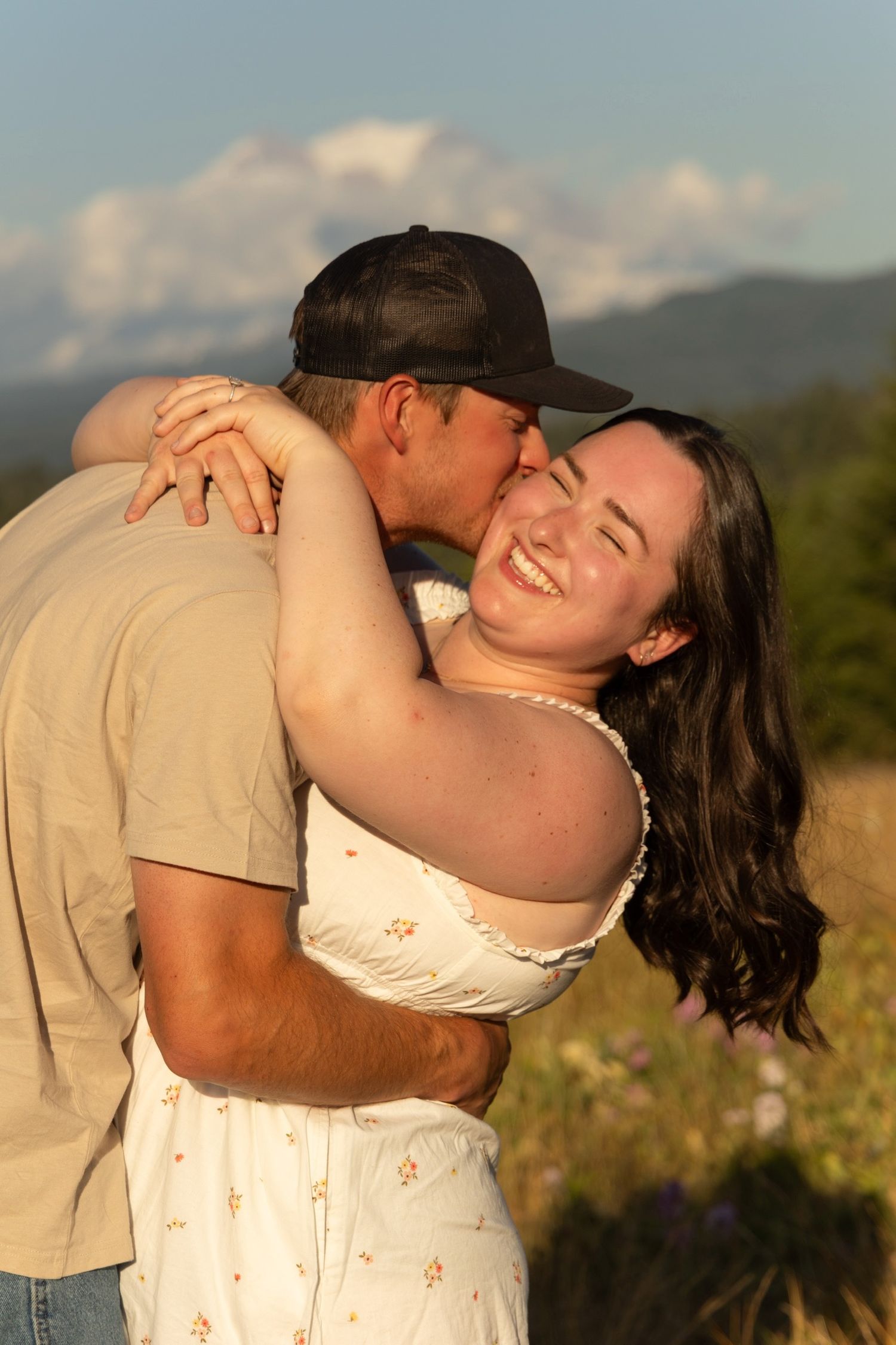 Joyful couple embracing in a sunny wildflower meadow with mountain views.