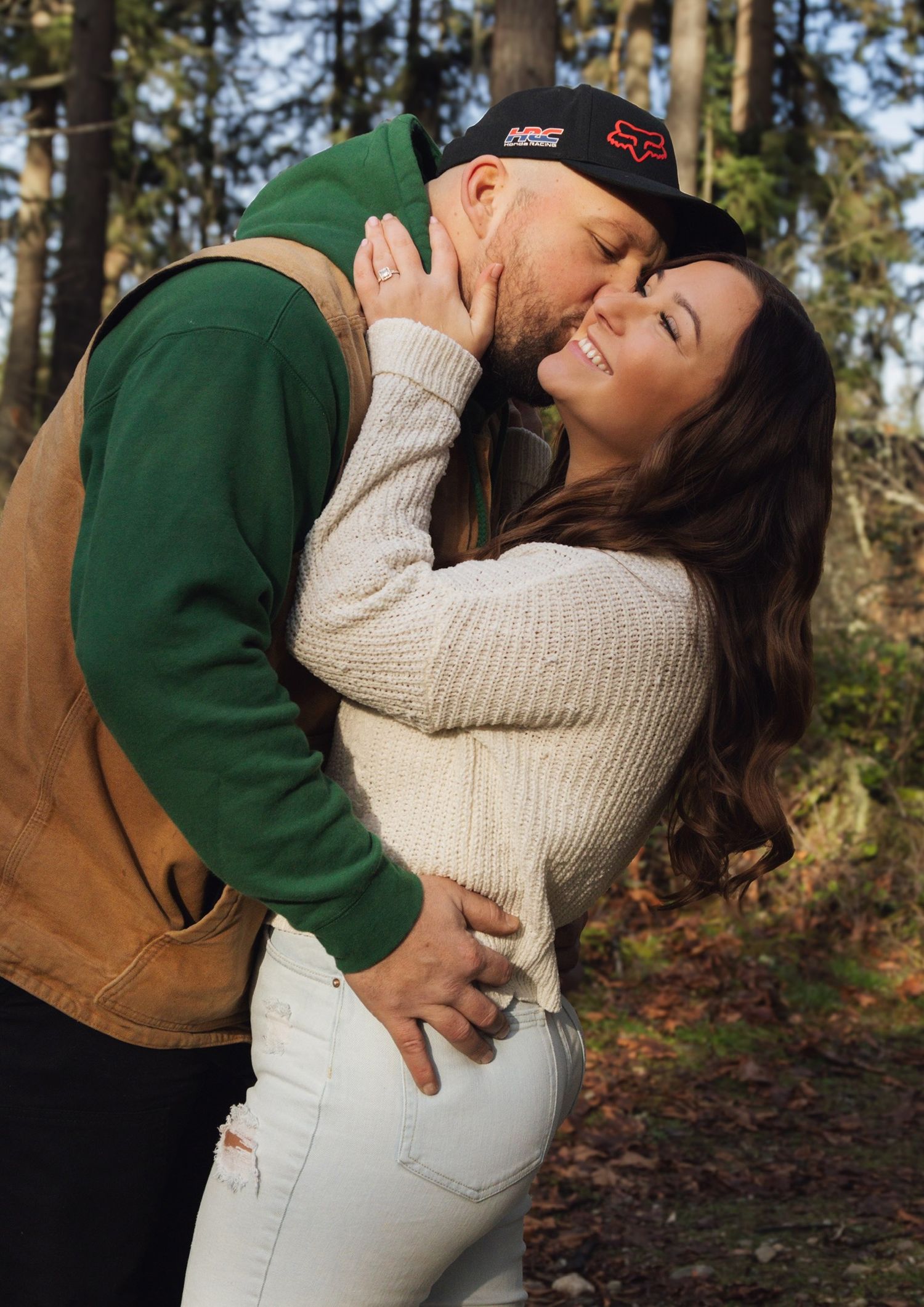 A romantic couple poses against a forest backdrop in casual autumn attire.