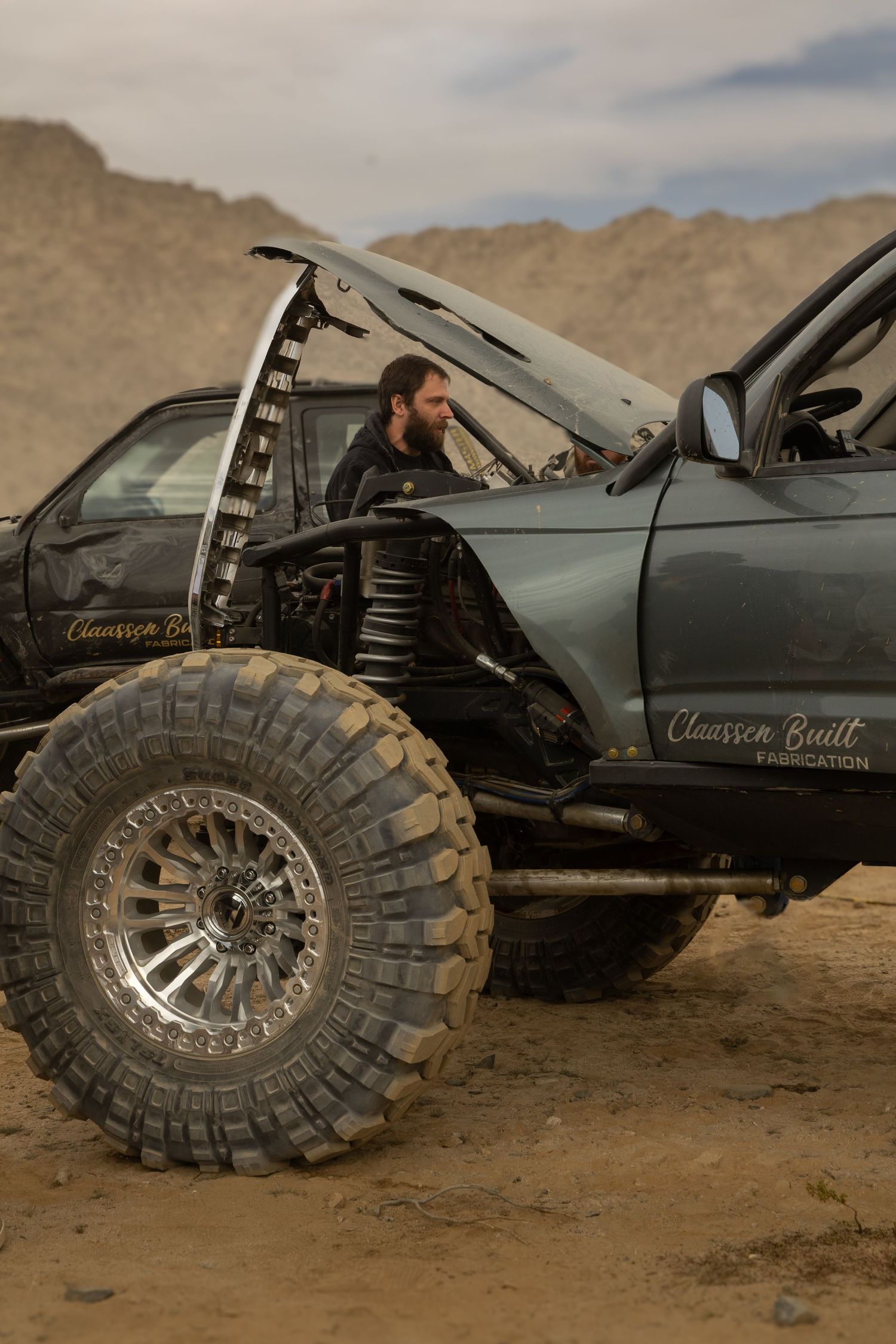 Off-road vehicle with large rugged tires being worked on in a desert landscape.