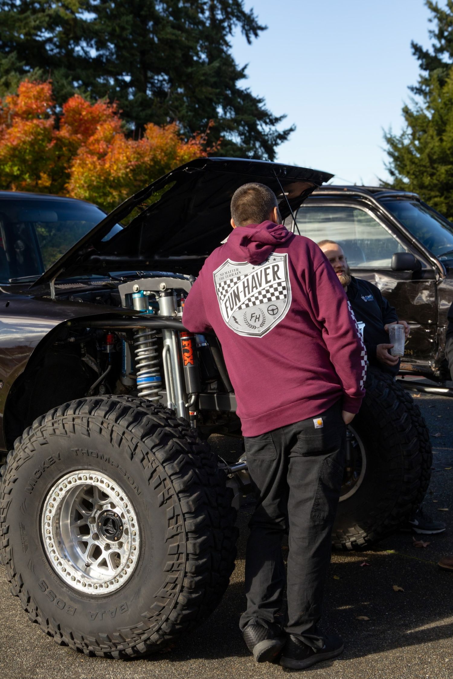 Off-road vehicle with large tires and burgundy apparel details shown in autumn outdoor setting.