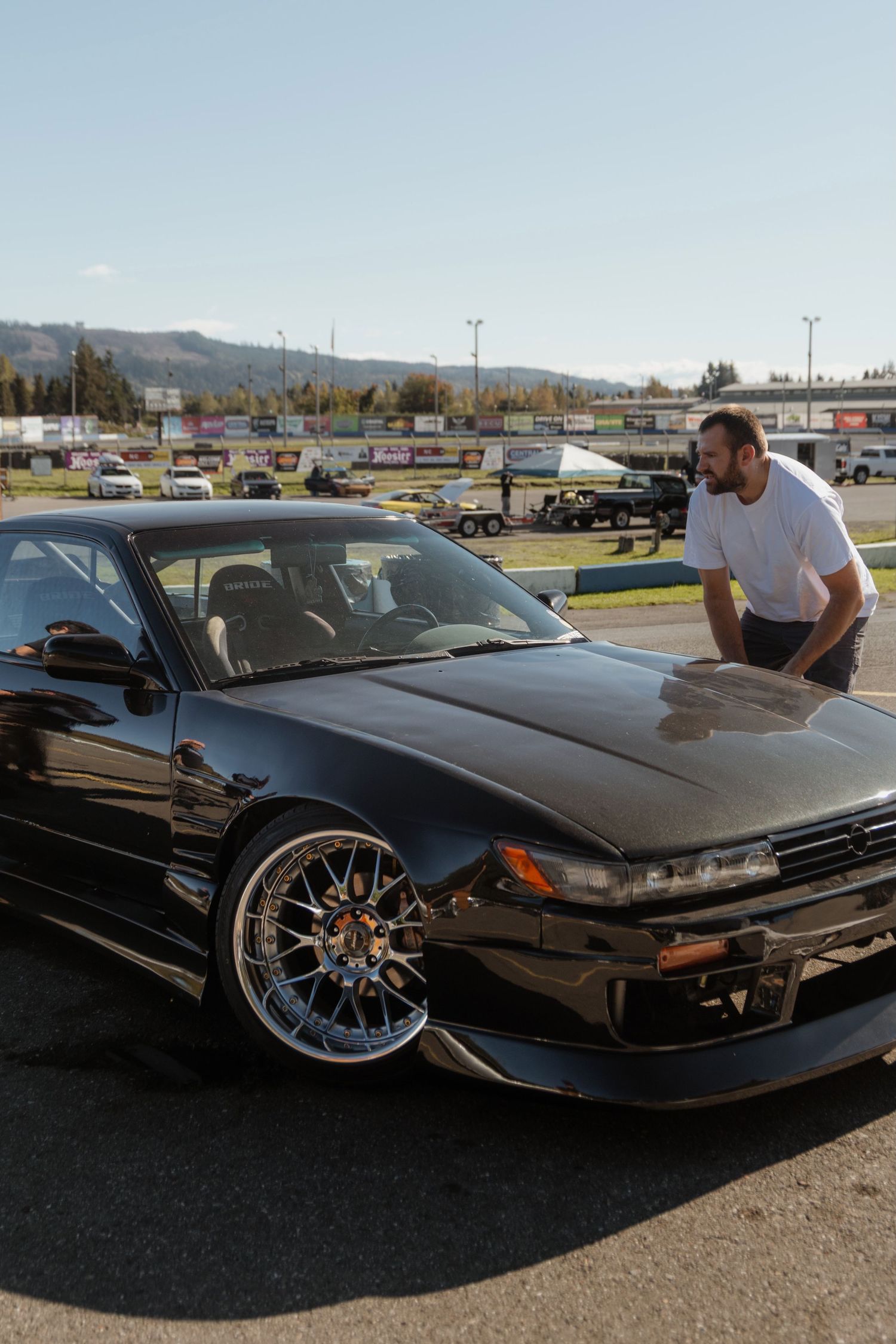 Black Nissan Silvia S13 with custom wheels parked in a lot with mountains visible in the background.
