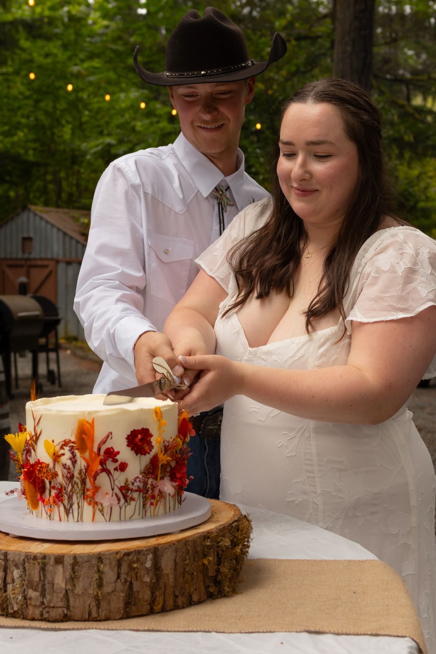 A couple cutting their autumn-themed wedding cake decorated with dried flowers on a wooden slice.