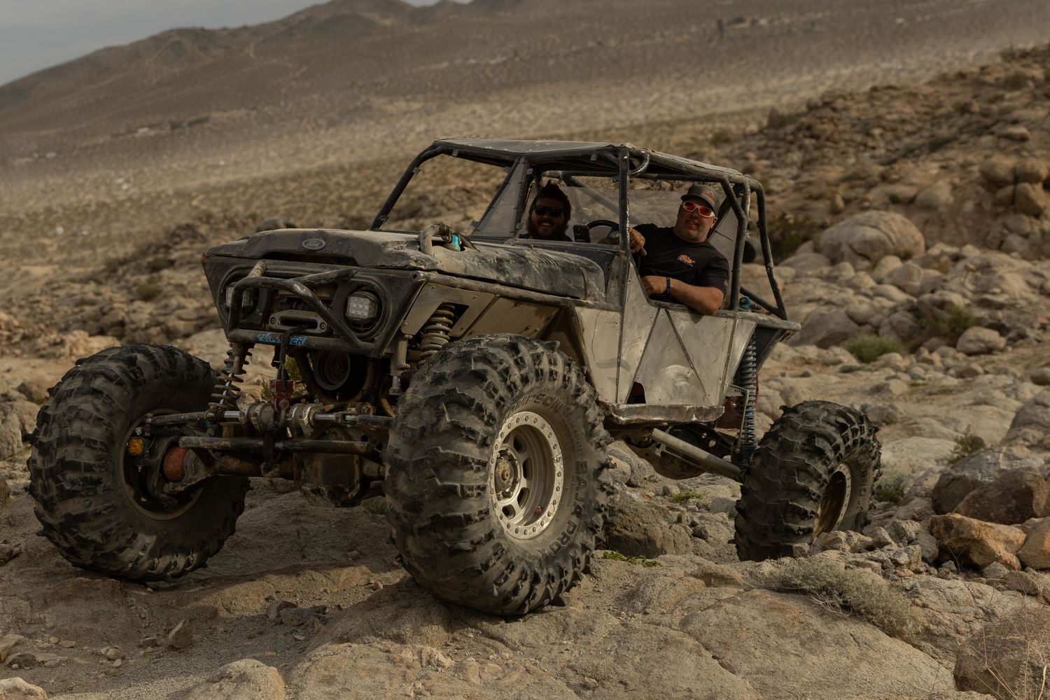 Custom off-road vehicles climbing over rugged desert rocks and boulders.