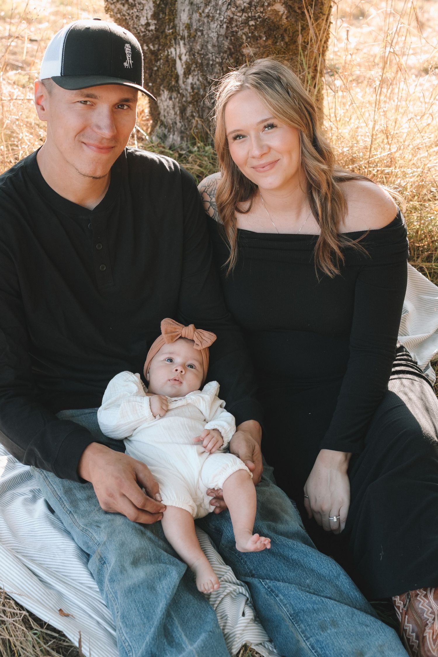 A family poses with their newborn baby in matching black and denim outfits during a casual photo session.