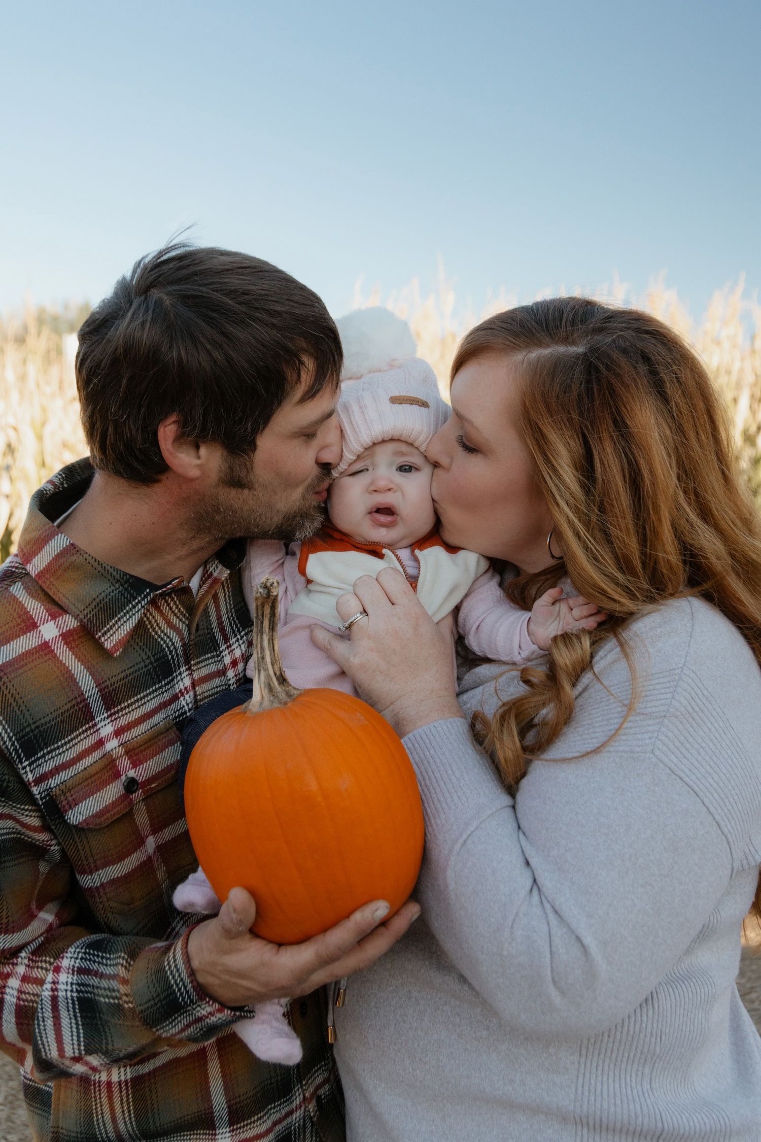 A family shares tender moments with their baby next to a bright orange pumpkin.