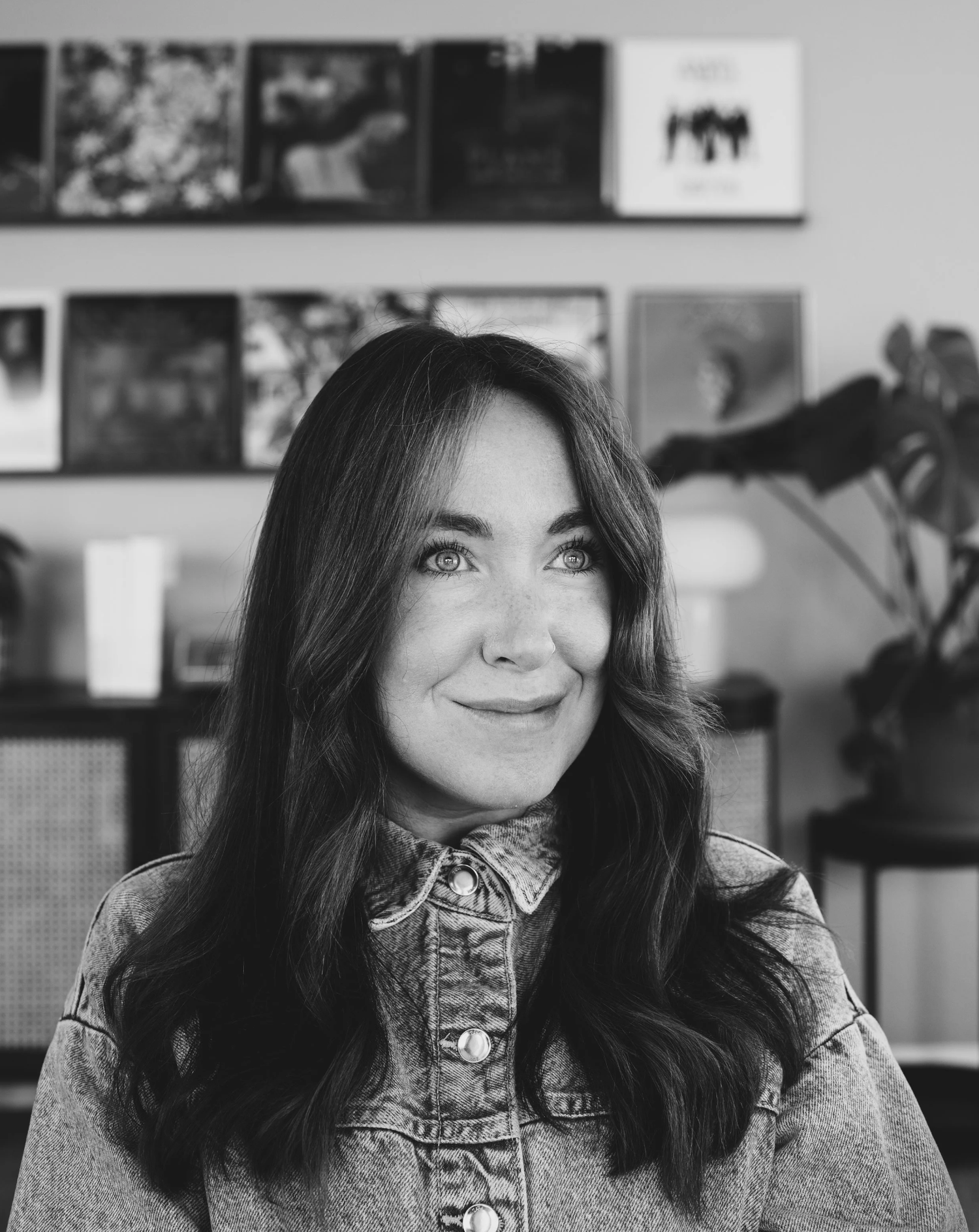 Black and white portrait of a smiling woman with long dark hair in a denim jacket with vinyl records behind her.