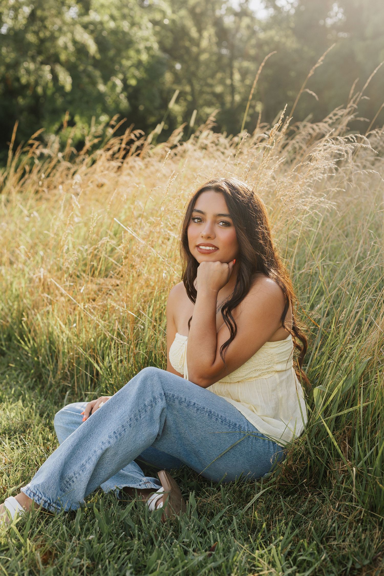 Casual outdoor portrait session in a sunlit field with tall grass and denim jeans.