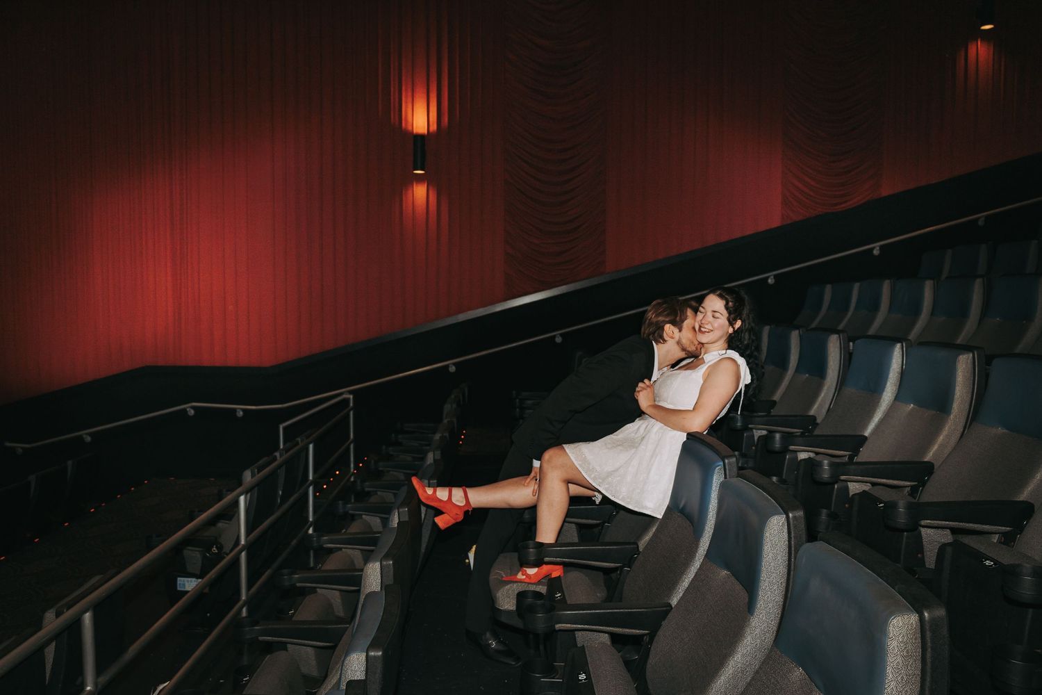 Romantic couple sharing intimate moment in dark movie theater seating.