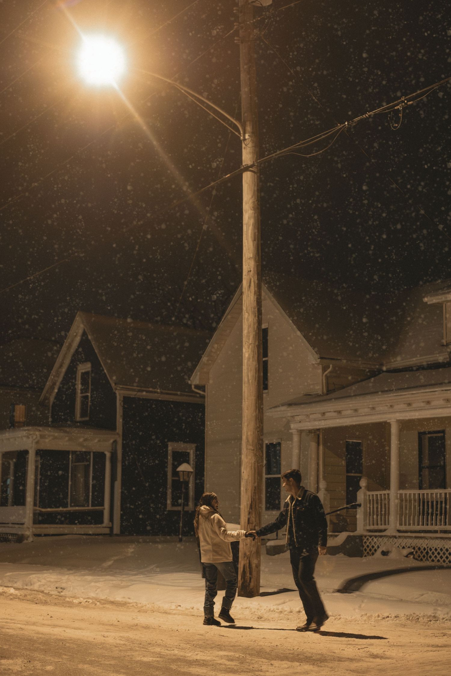Snowy nighttime street scene with streetlamp illuminating houses.