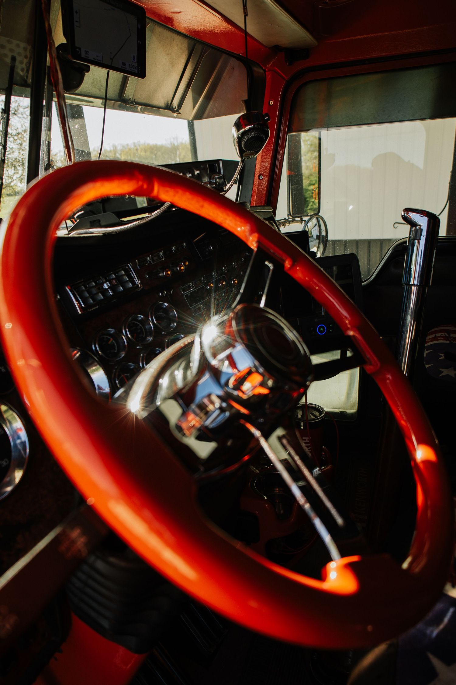 Interior view of semi truck dashboard with illuminated red steering wheel.