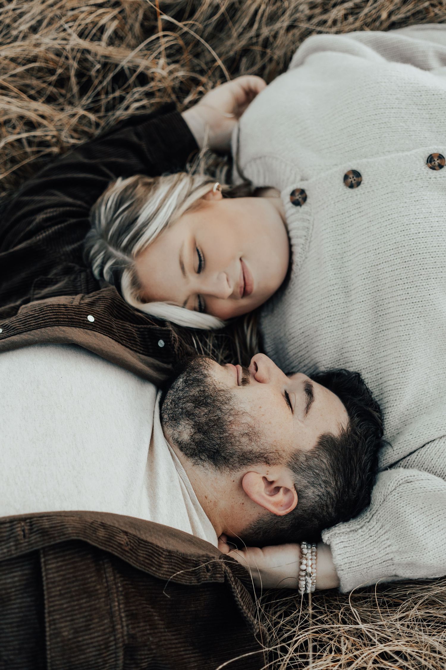 Couple lying together in dry grass during intimate outdoor photo session.