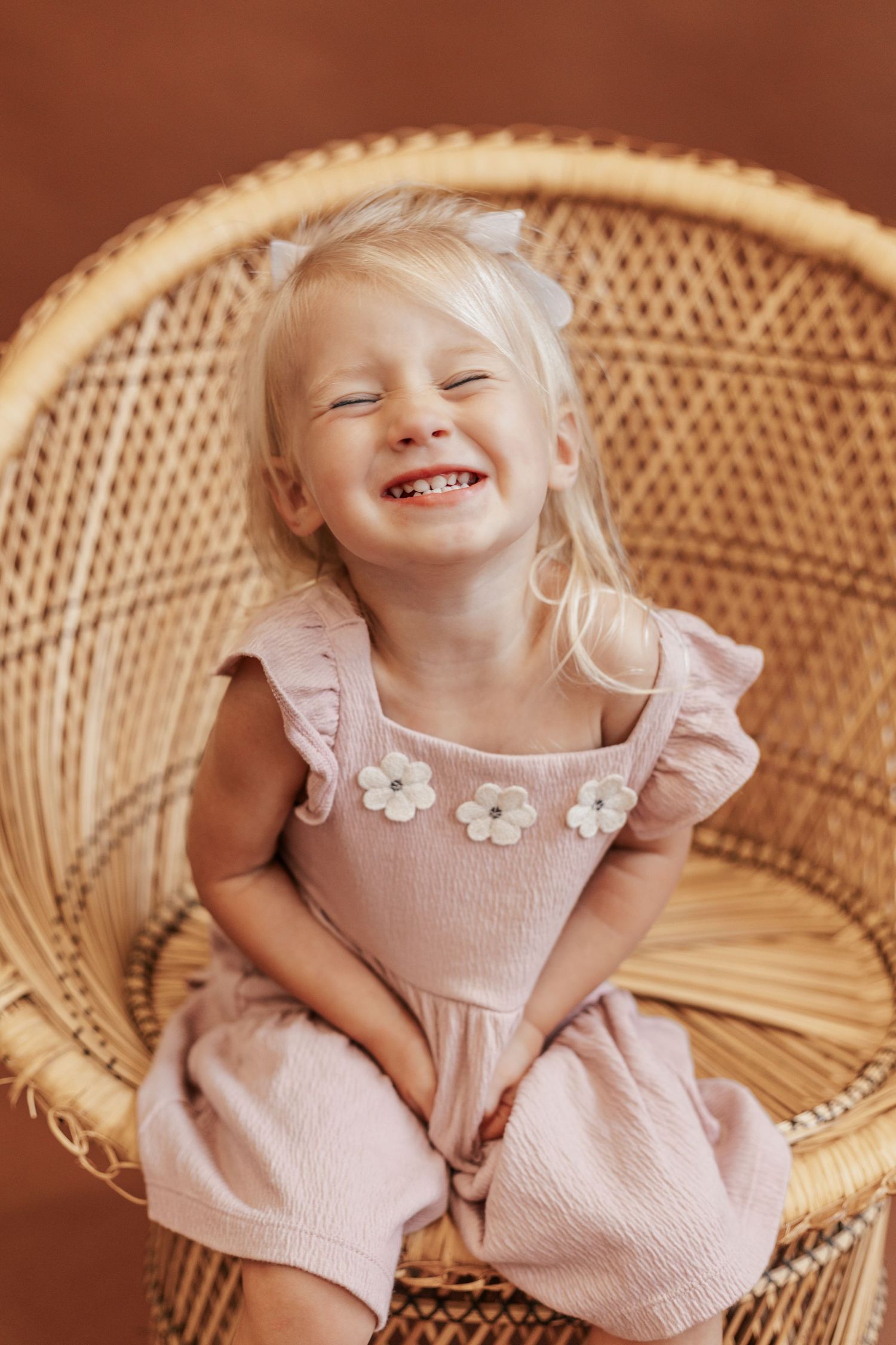 A pink dress-clad figure resting in a woven peacock chair against a warm brown background.