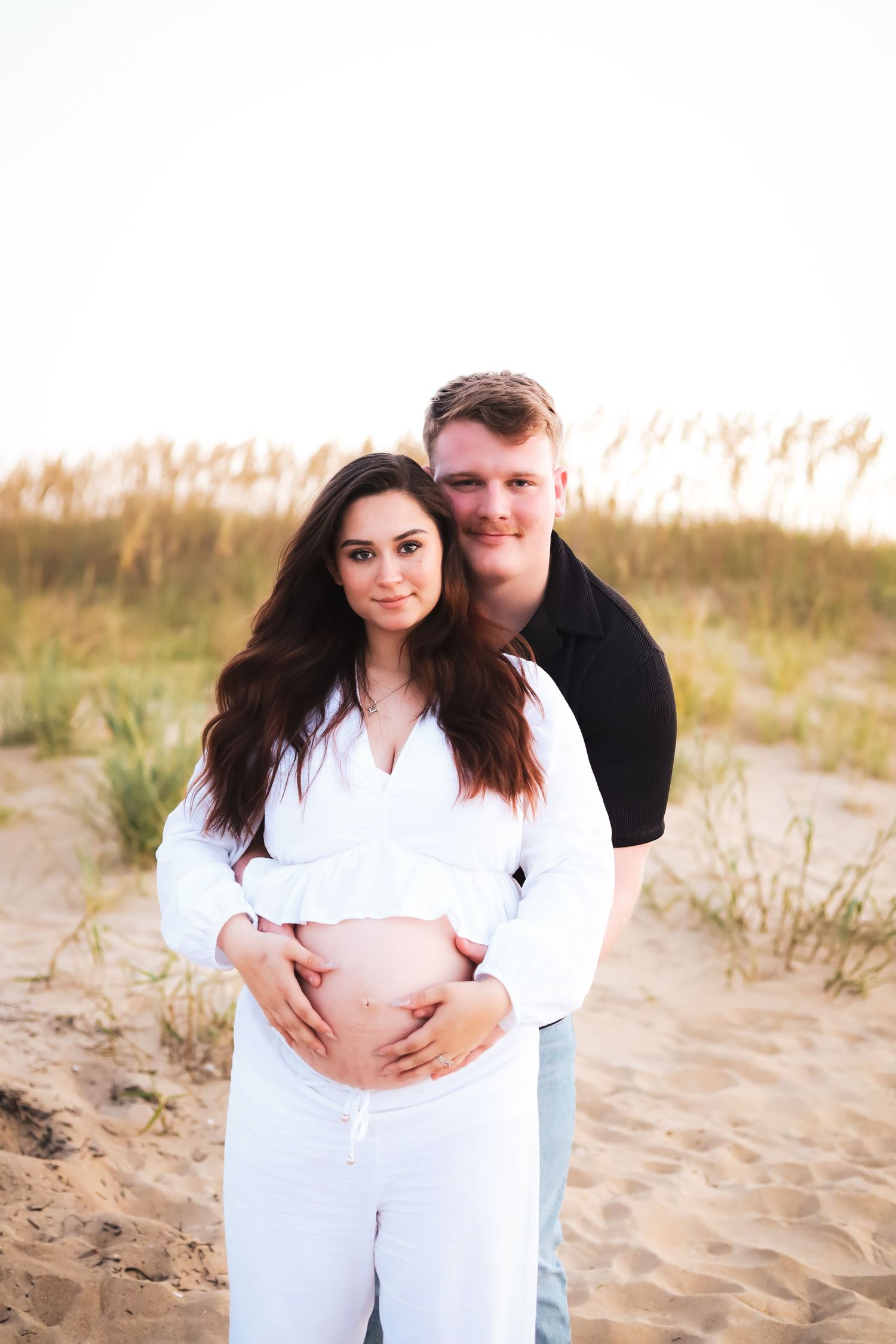 Couple embracing during beach maternity photoshoot at golden hour.