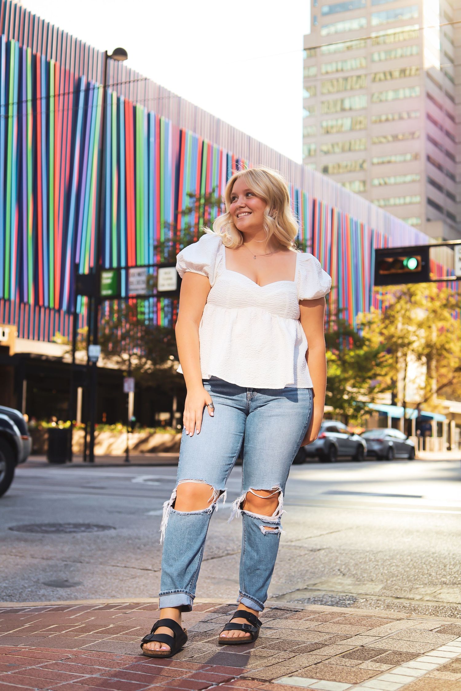 Person in casual outfit poses near colorful striped wall in city environment.