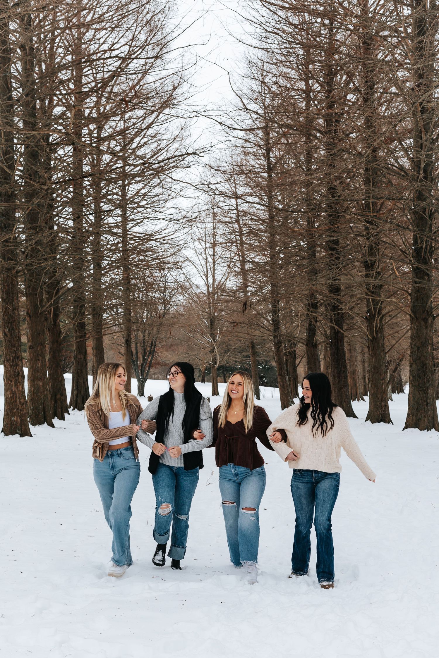 Friends walking together through a snow-covered forest path in casual winter attire.