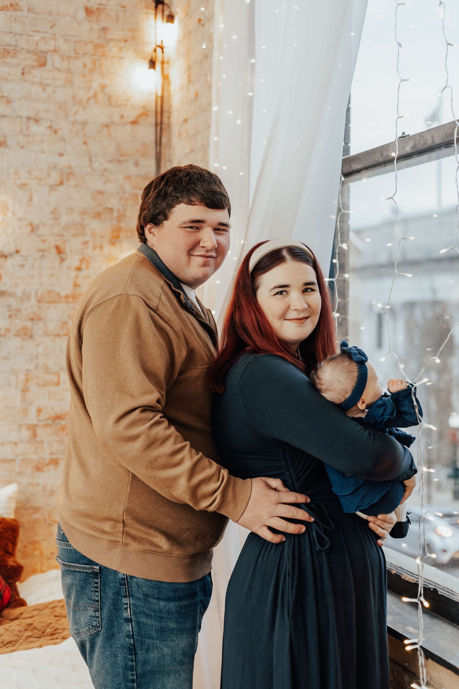 Couple sharing intimate embrace against brick wall with string lights.