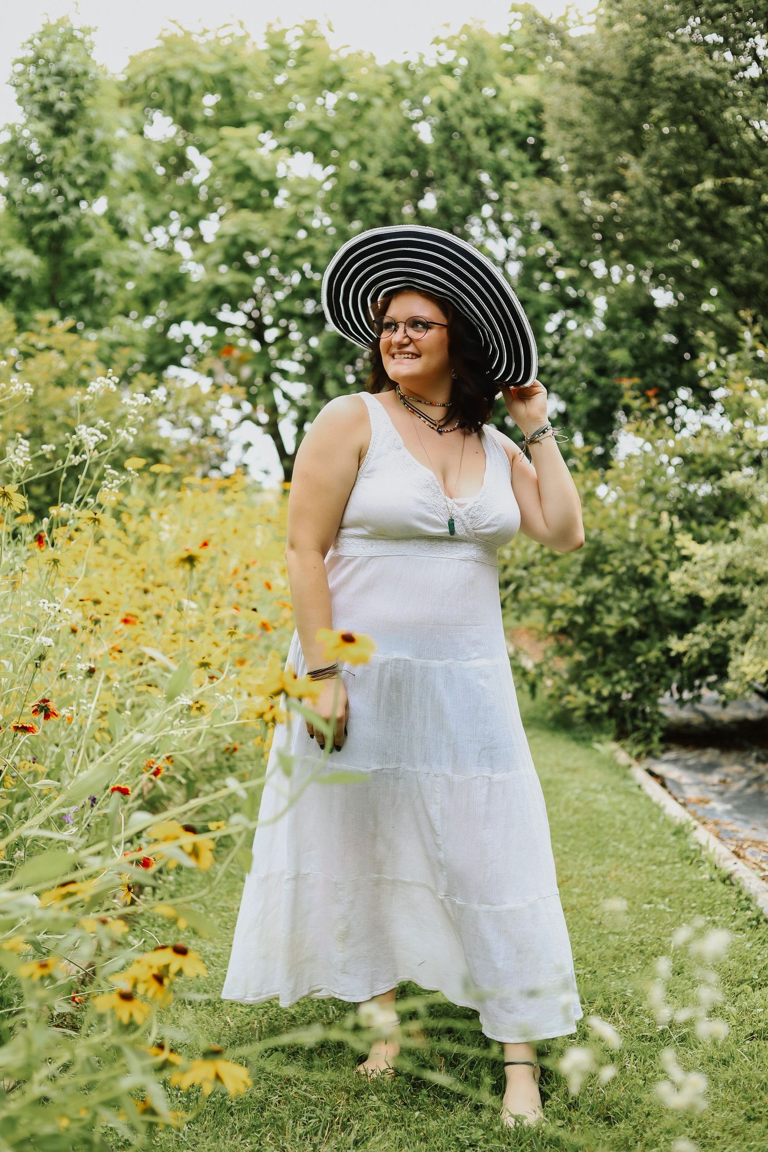 A white dress and black sun hat create contrast against yellow wildflowers in a summer garden.