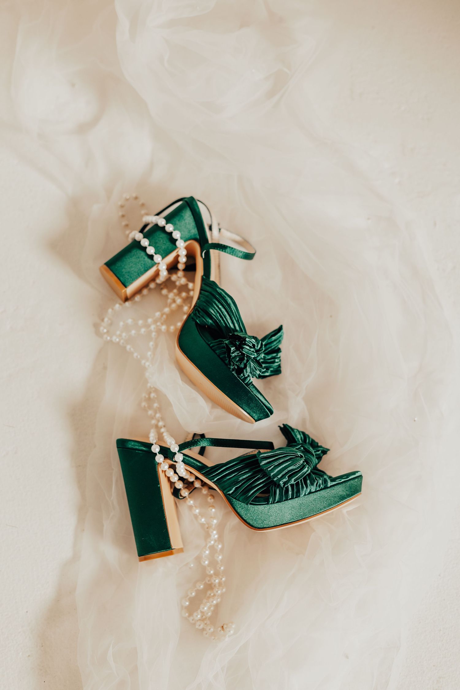Vintage-inspired emerald green heels with pearls on cream background.
