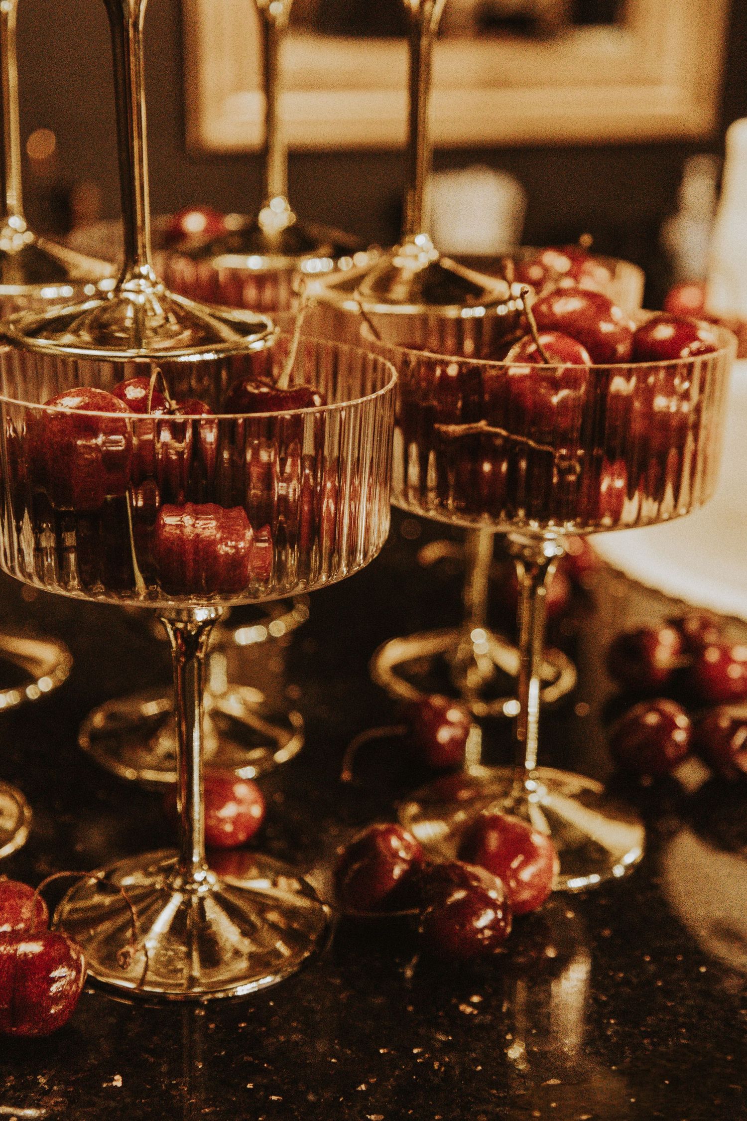 Crystal coupe glasses filled with fresh cherries in warm ambient lighting.