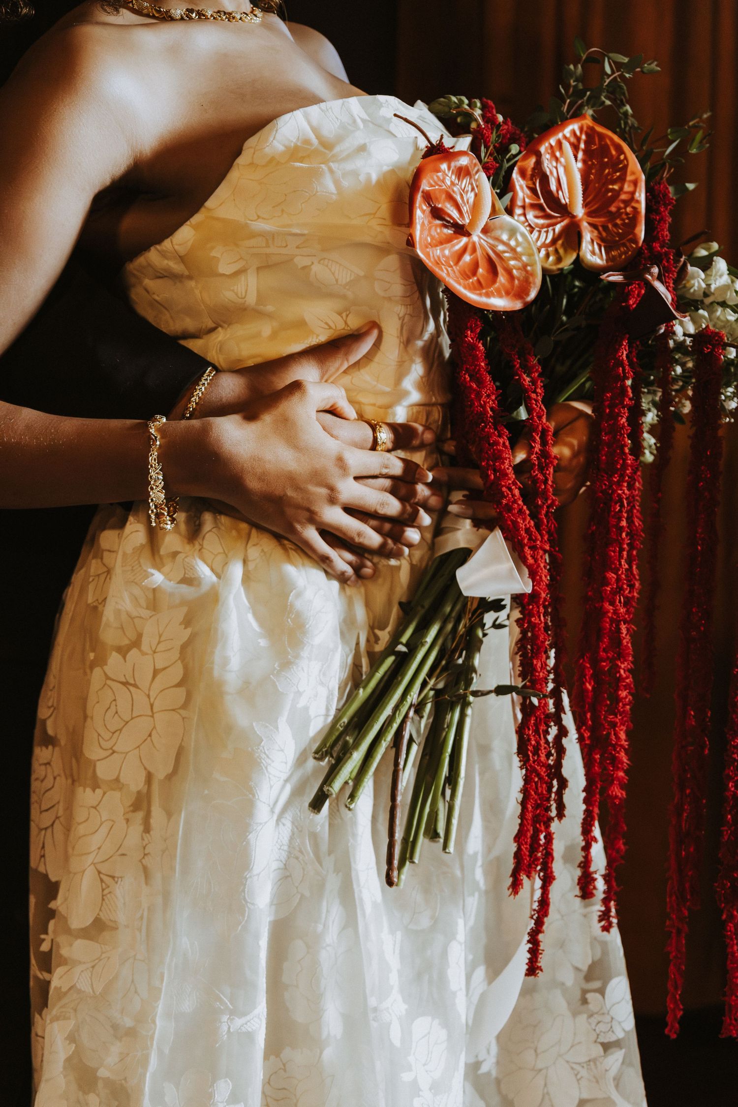 Close-up of white wedding dress with citrus and red amaranthus bouquet details.