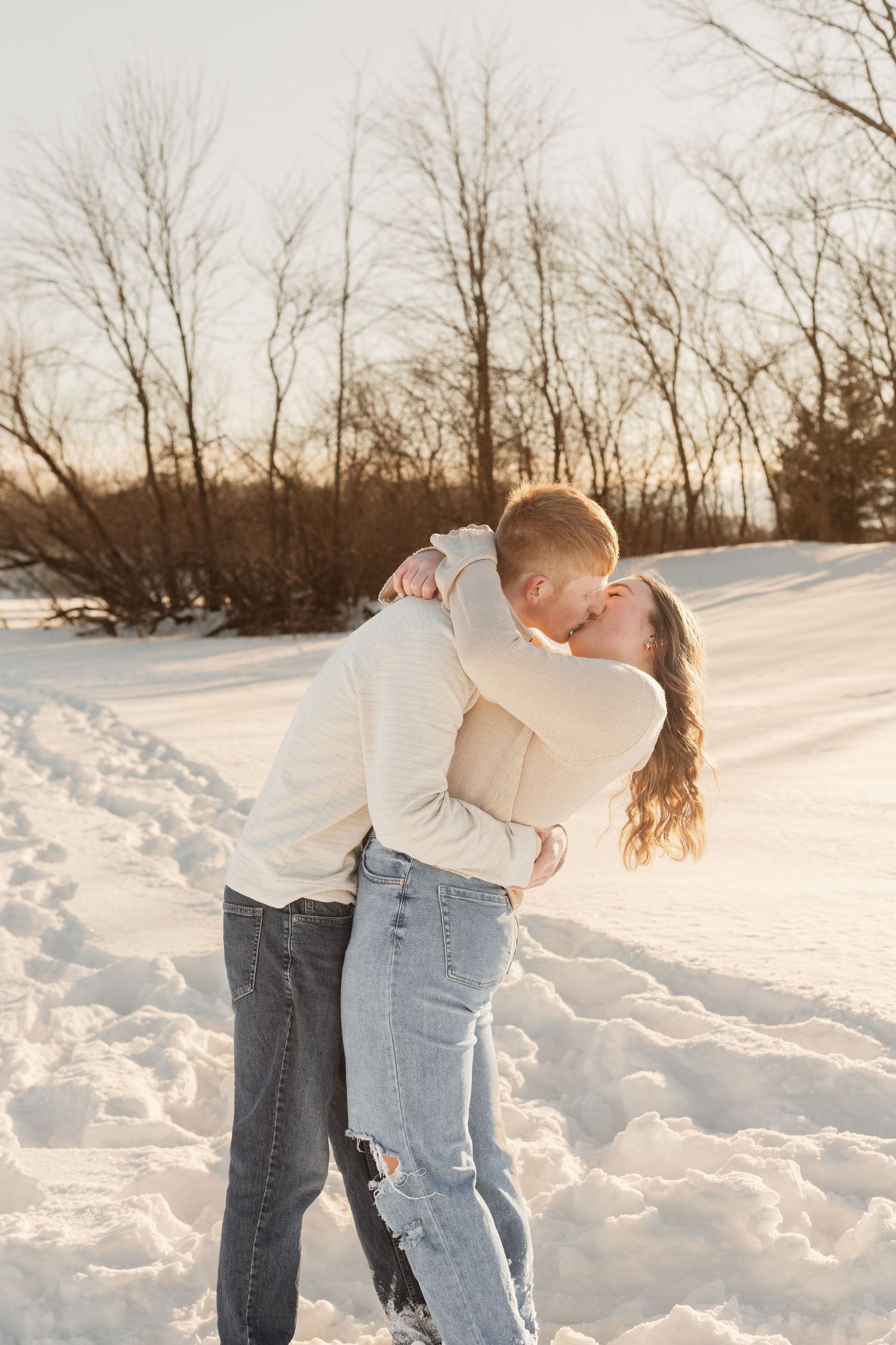 A romantic winter embrace between a couple in casual clothing against a snowy backdrop.