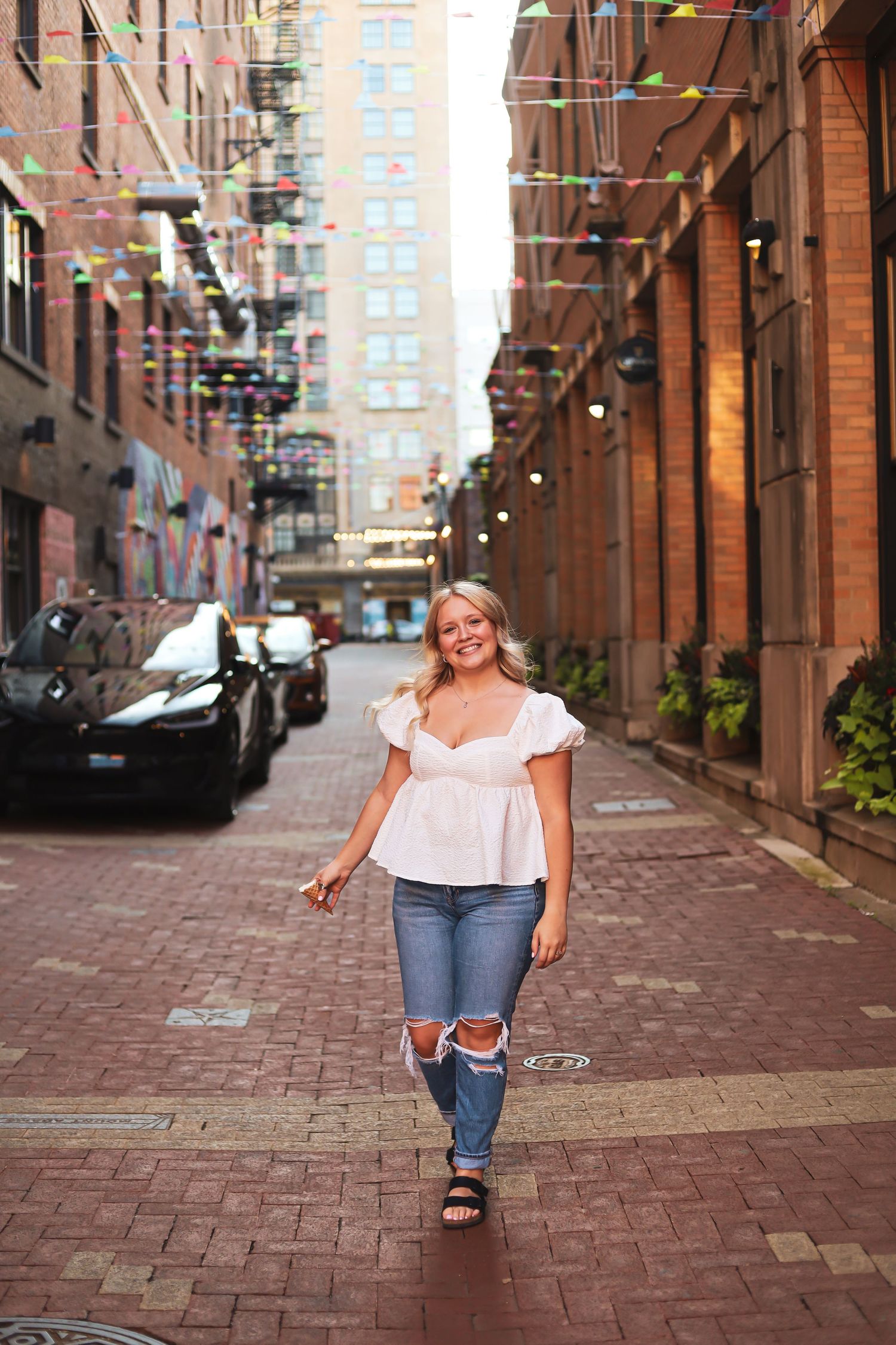 Person walking and posing on brick-paved alley between historic buildings.