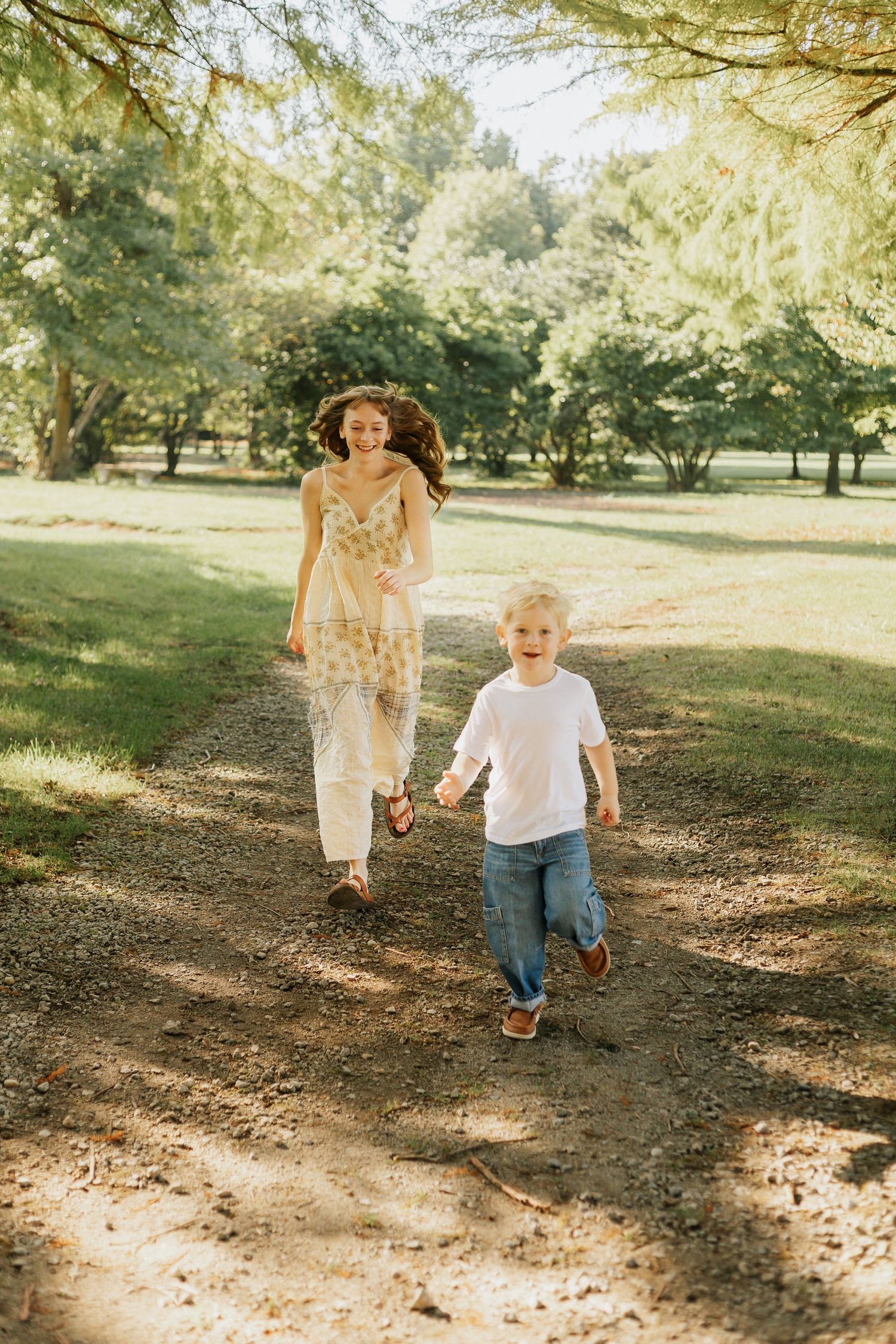 Family running and playing together on tree-lined path in sunlit park.