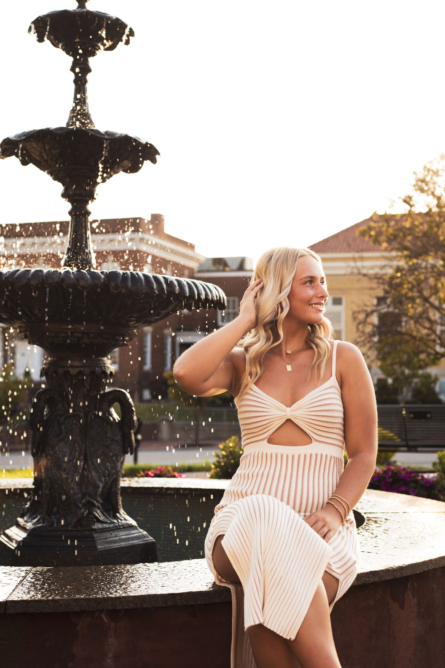 Woman in striped dress poses by ornate fountain in evening light.