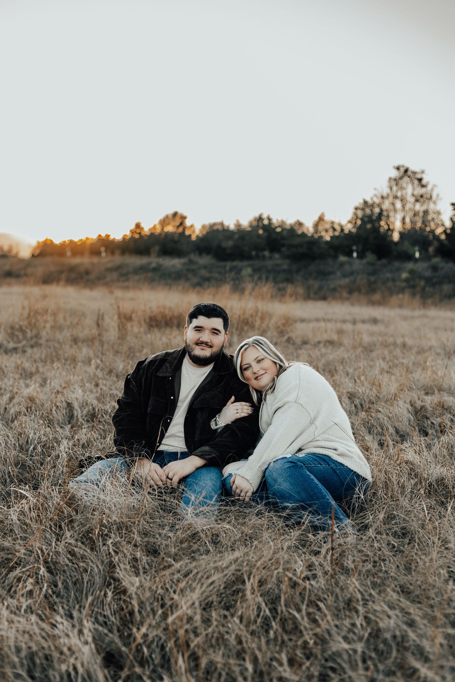 Couple relaxing in golden autumn field during sunset photo session.