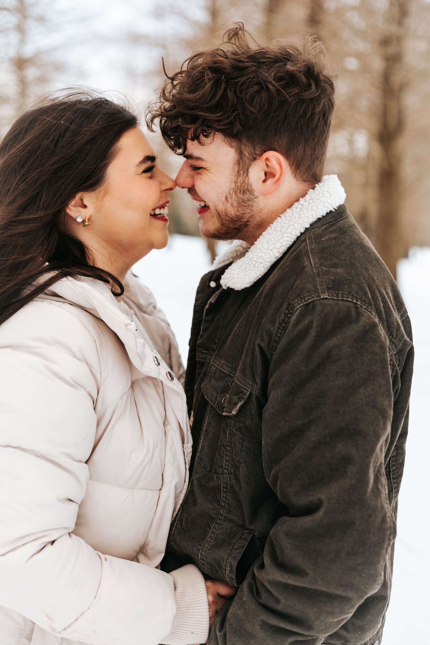 Couple sharing intimate winter moment in warm coats against snowy forest backdrop.