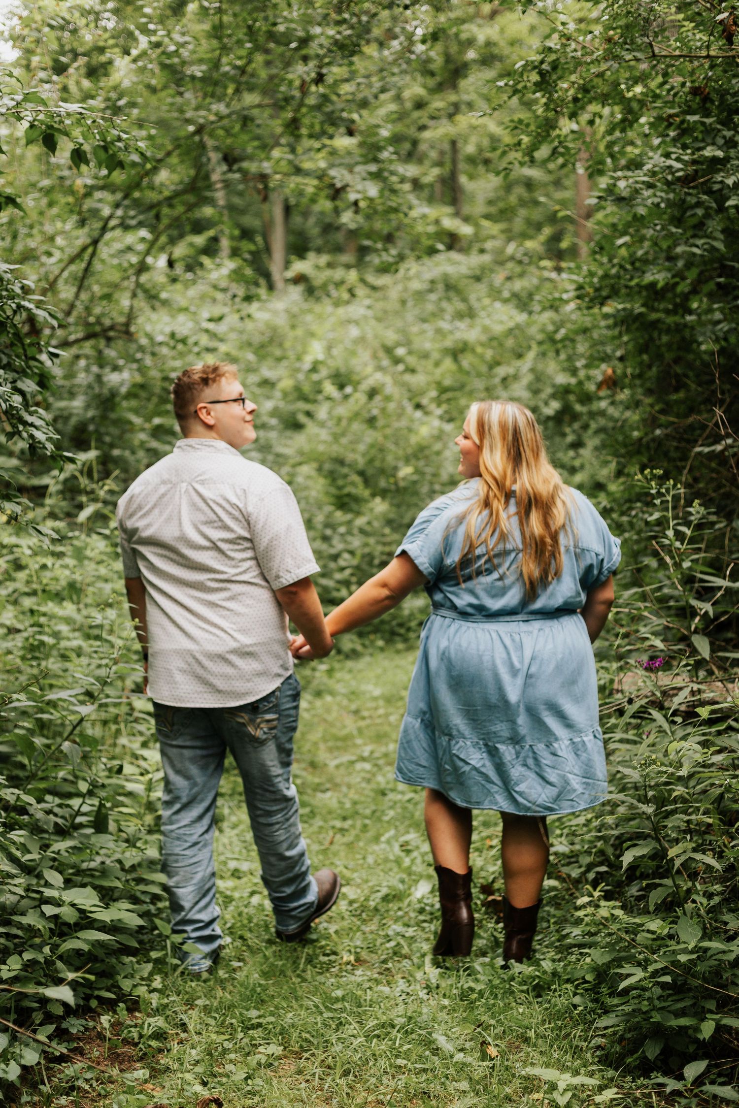 Couple walking hand in hand through lush green forest path.