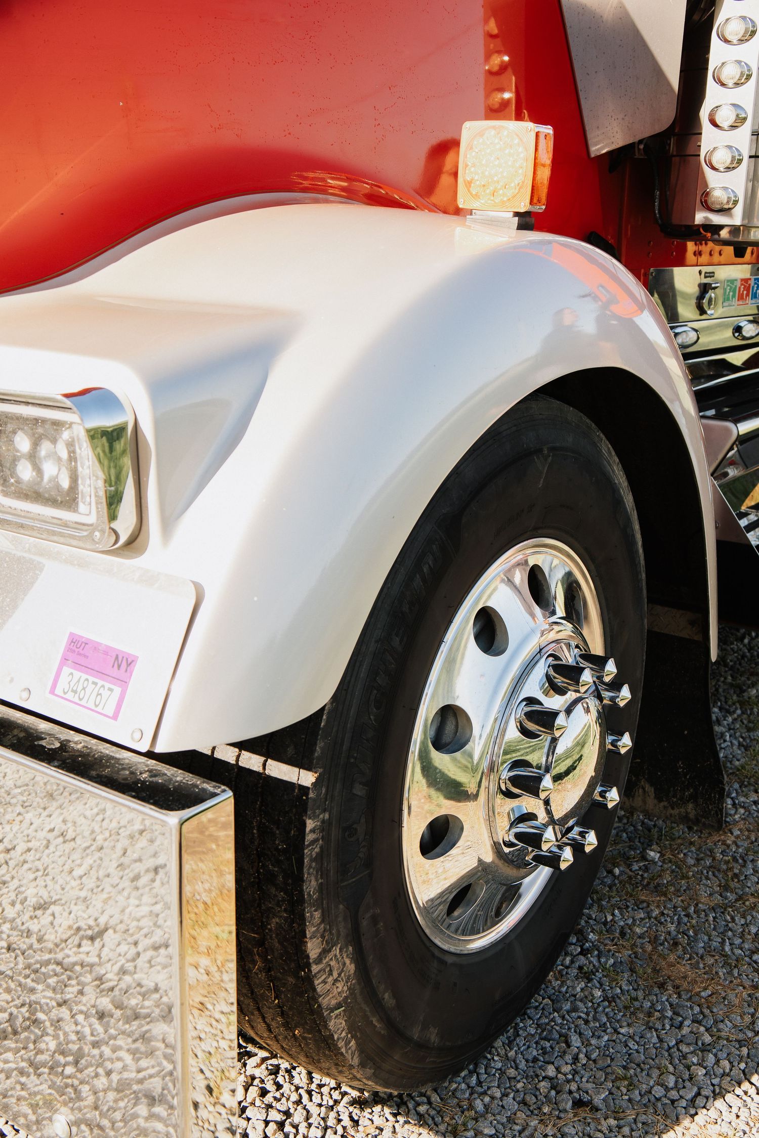 Close-up view of a chrome truck wheel and tire mounted on a white semi truck fender.