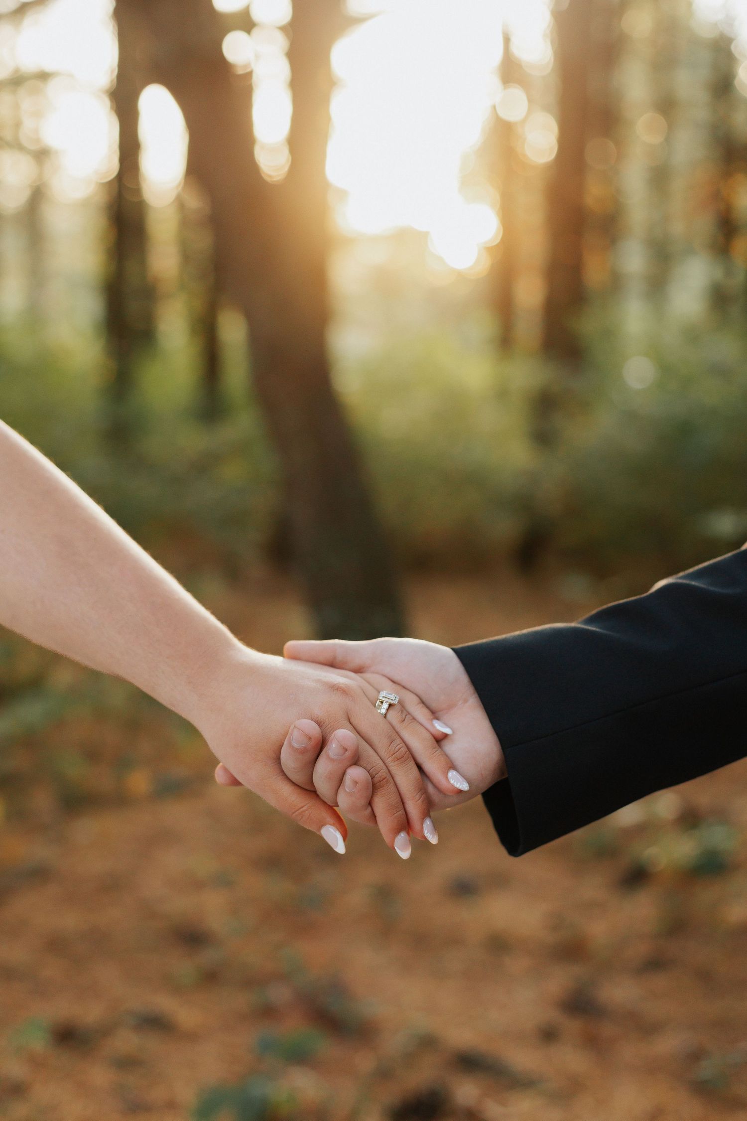 Close-up of newlyweds holding hands with wedding rings in golden sunset light.