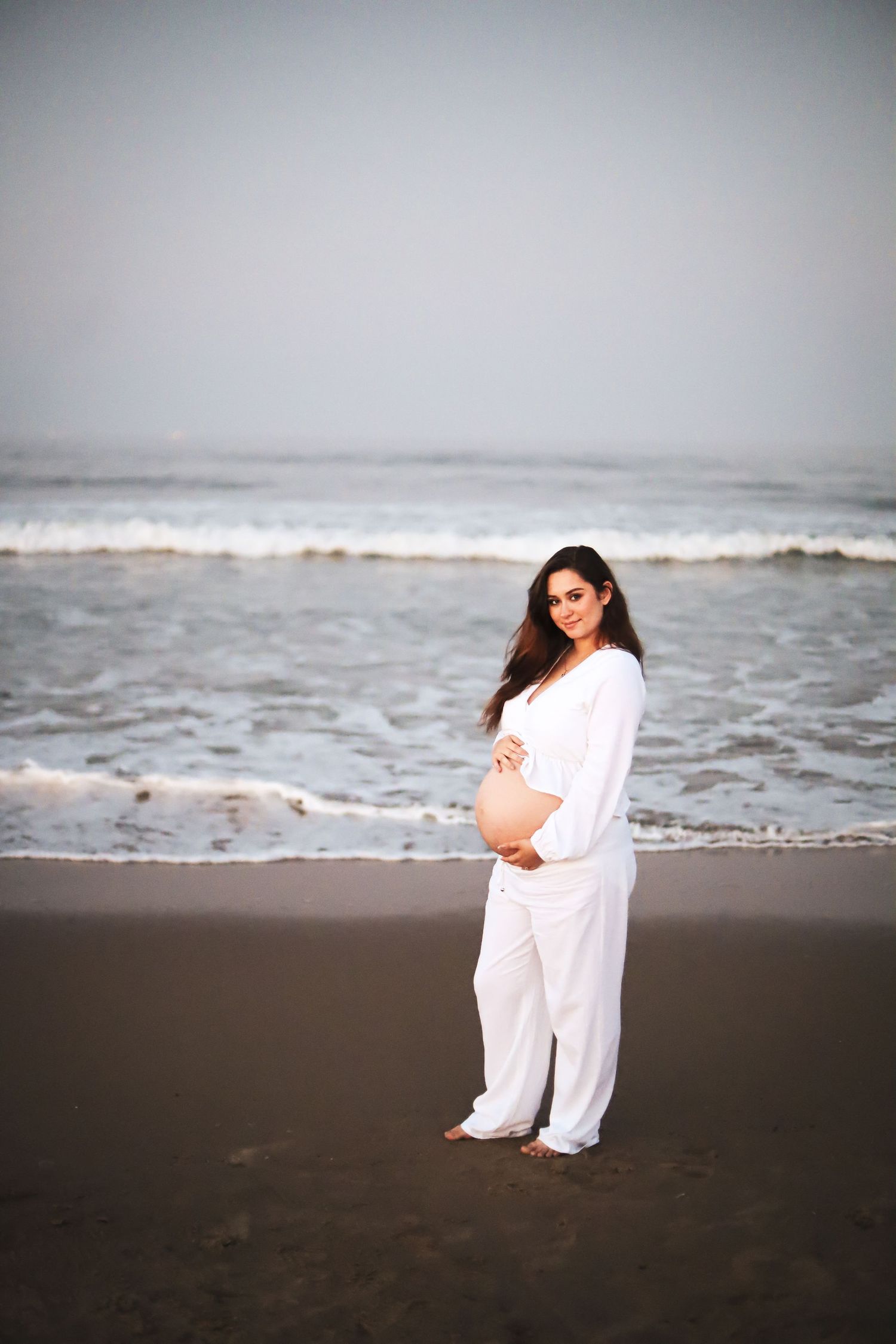 A series of beach maternity photos showing a person in white clothing against dark sand and ocean waves.