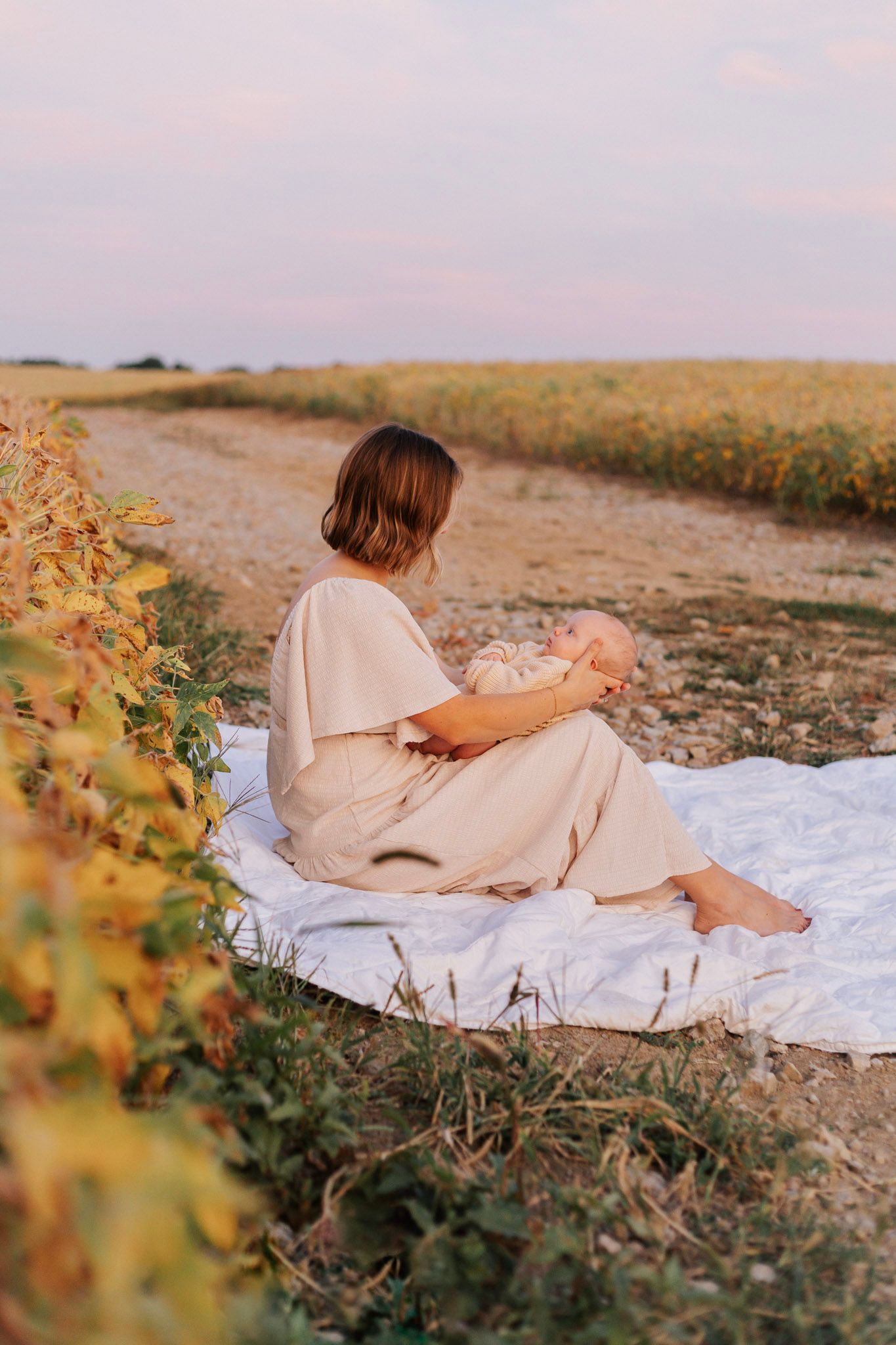 Mother and child resting on white blanket during sunset surrounded by wildflowers.