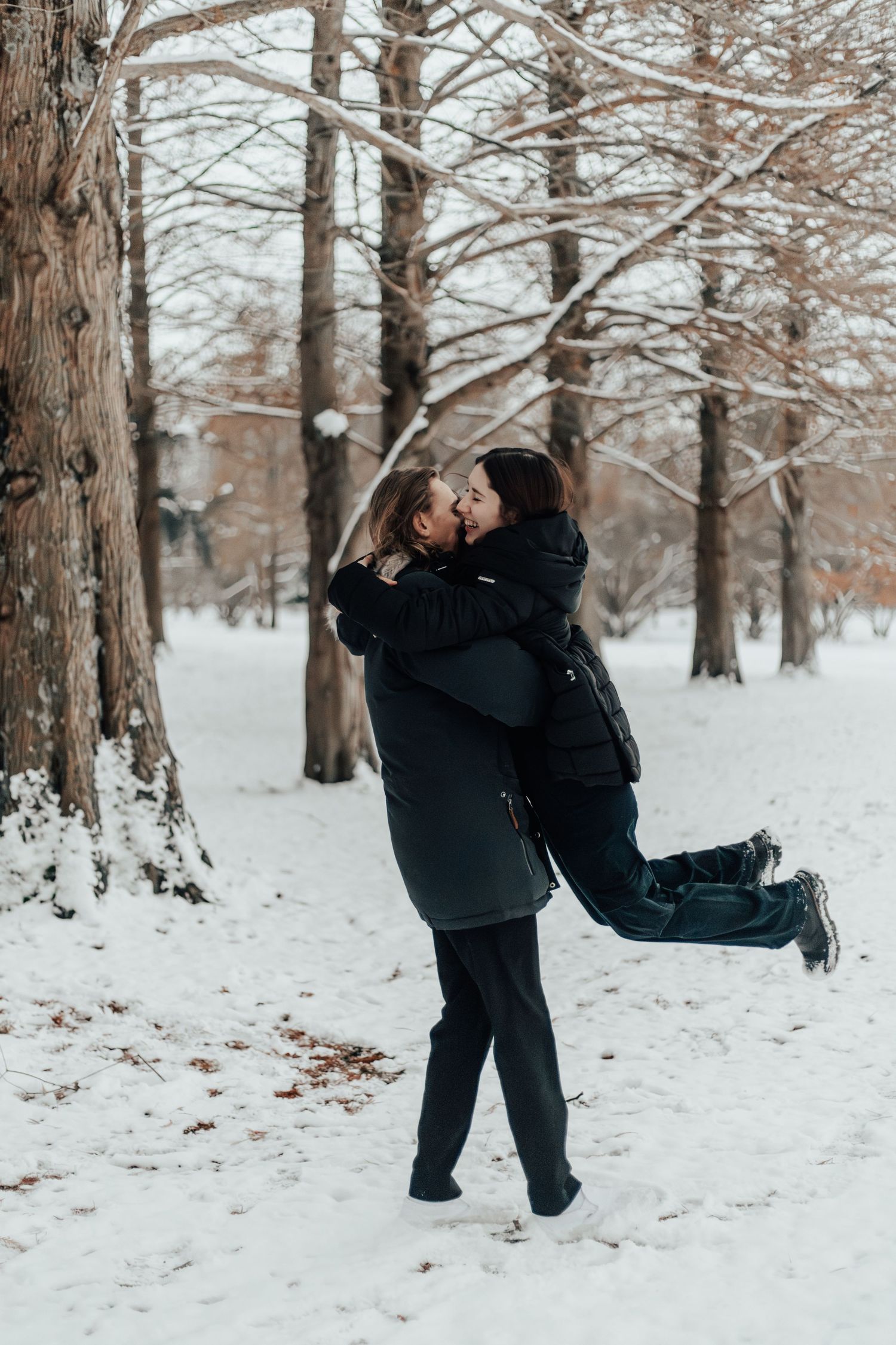 A romantic winter moment as a couple shares a playful lift in the snowy forest.