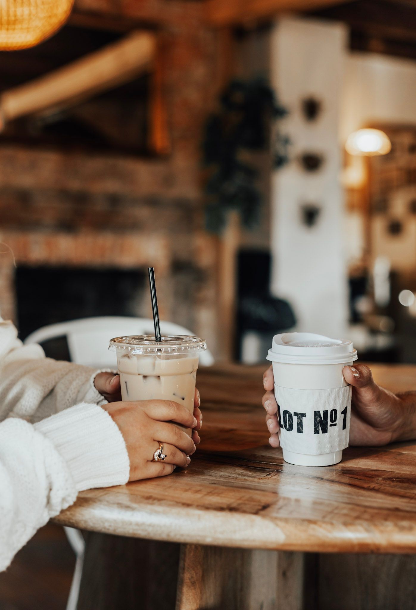 Coffee cups with text on them sitting on a rustic wooden table in a cafe setting.