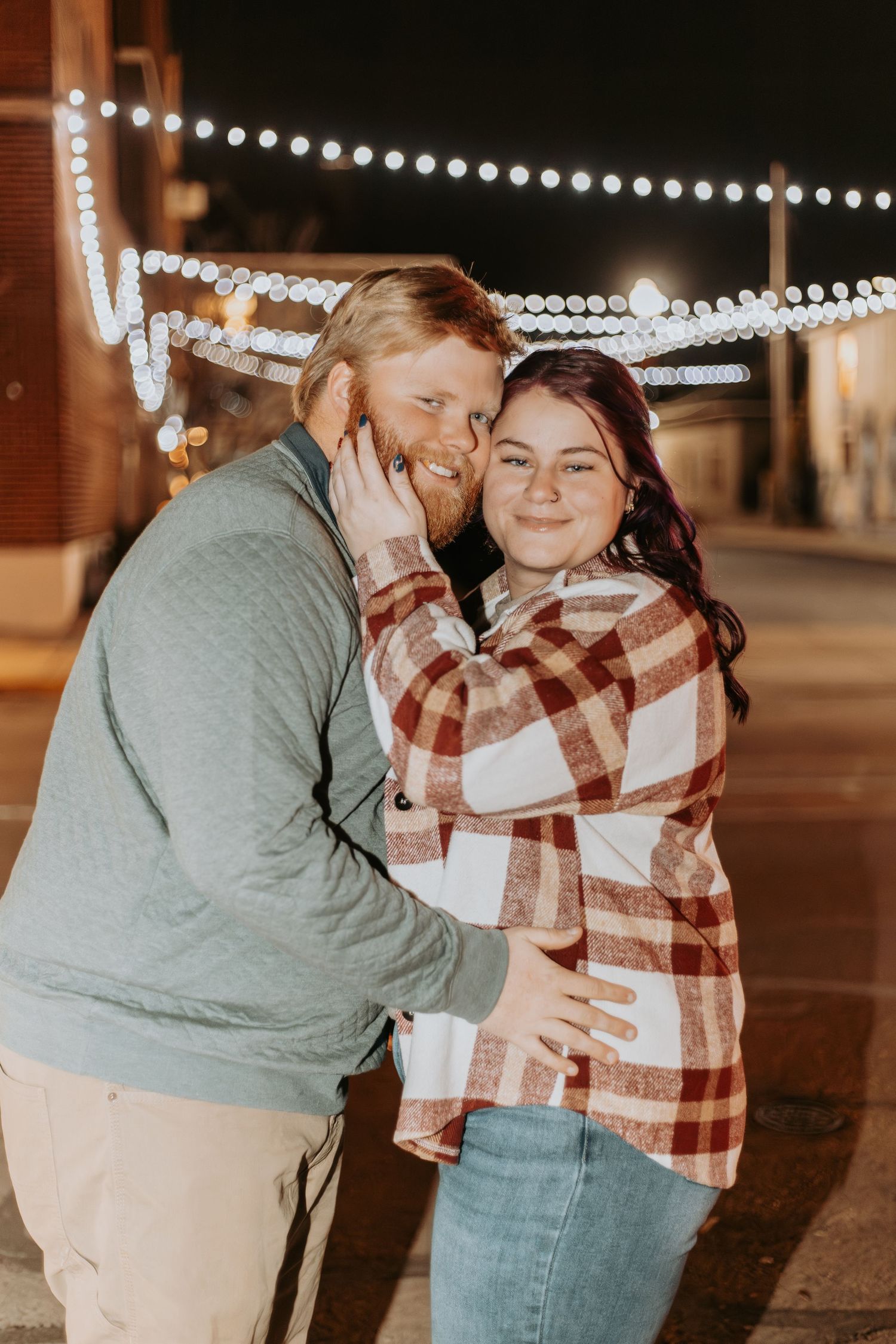 A couple shares a sweet moment under string lights at night.