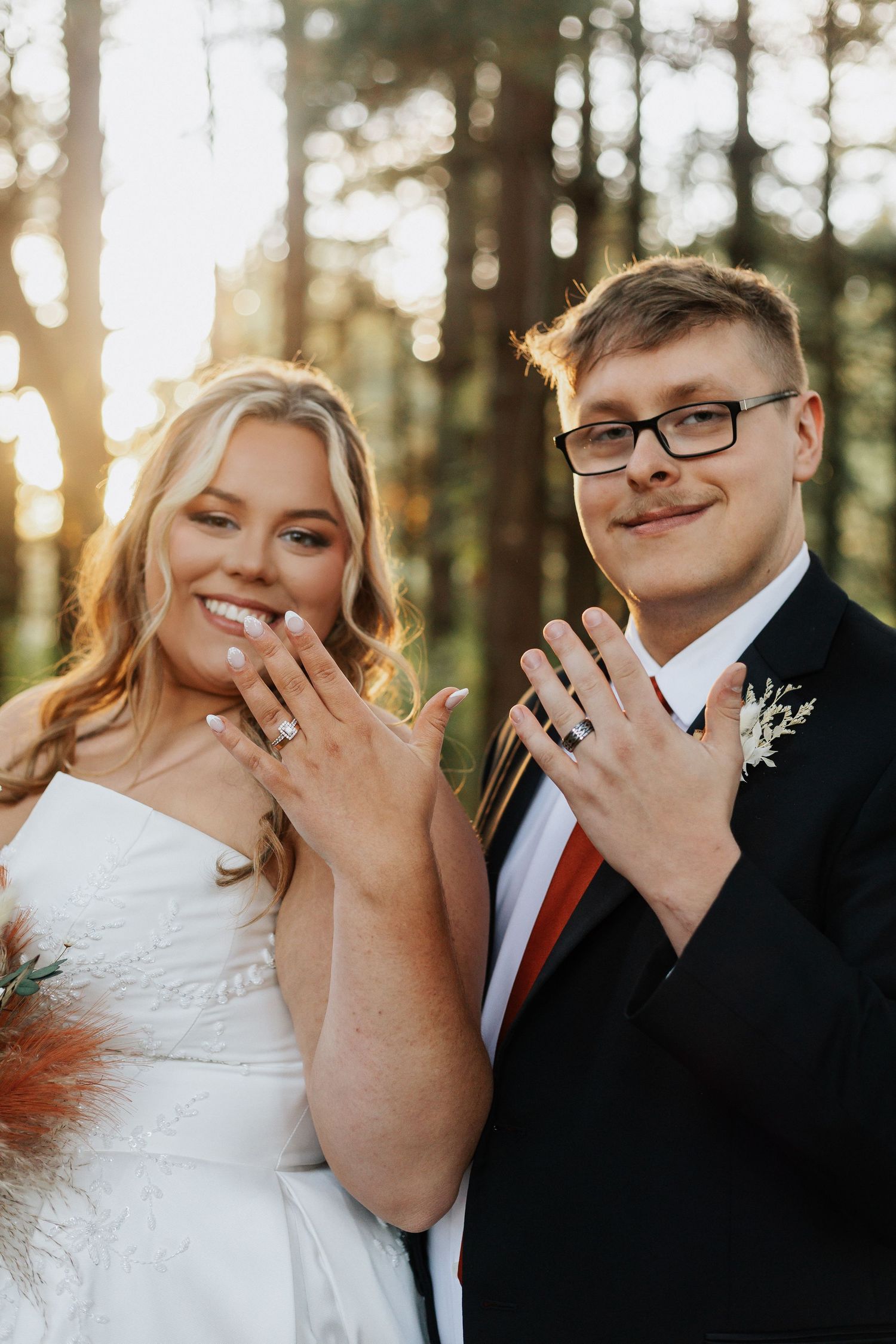 Close-up shot of couple showing off their wedding rings in a forest setting at sunset.