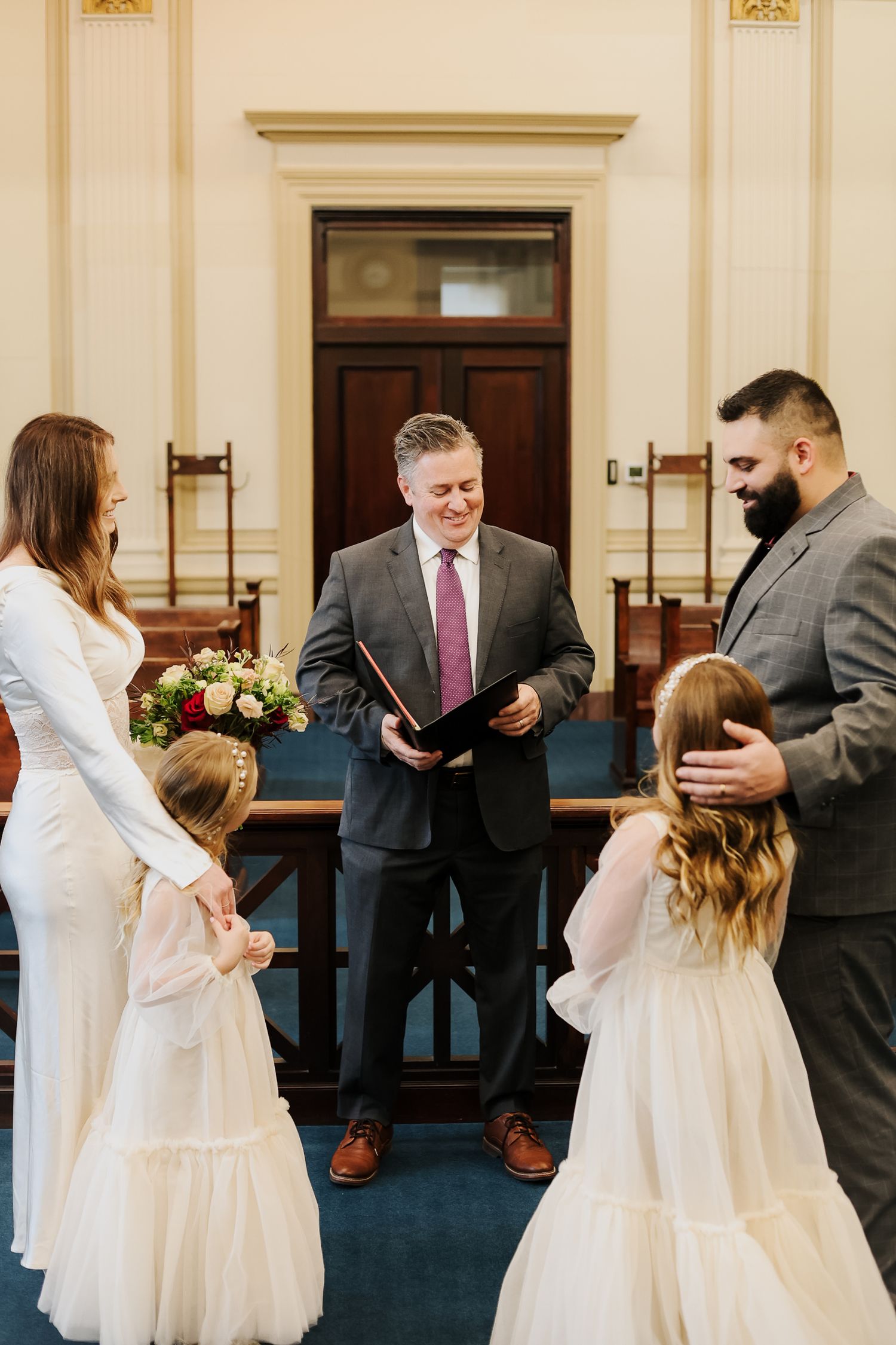 Wedding party members in formal attire interacting in a row along a blue carpeted hallway.
