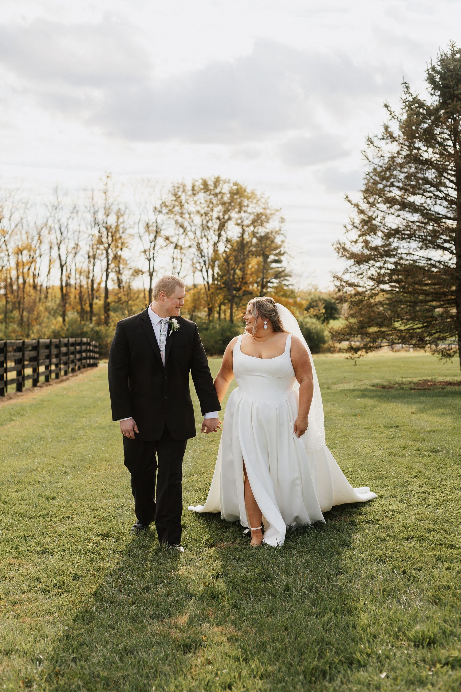 Couple walking across a grassy field during a wedding photoshoot at sunset.