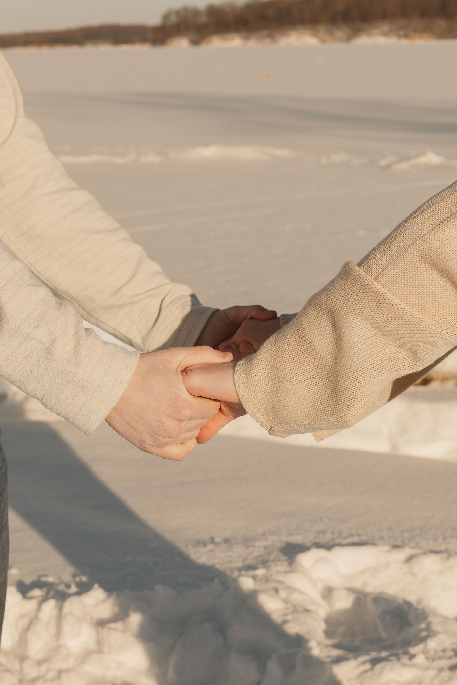 Close-up of hands holding each other against a snowy winter background.