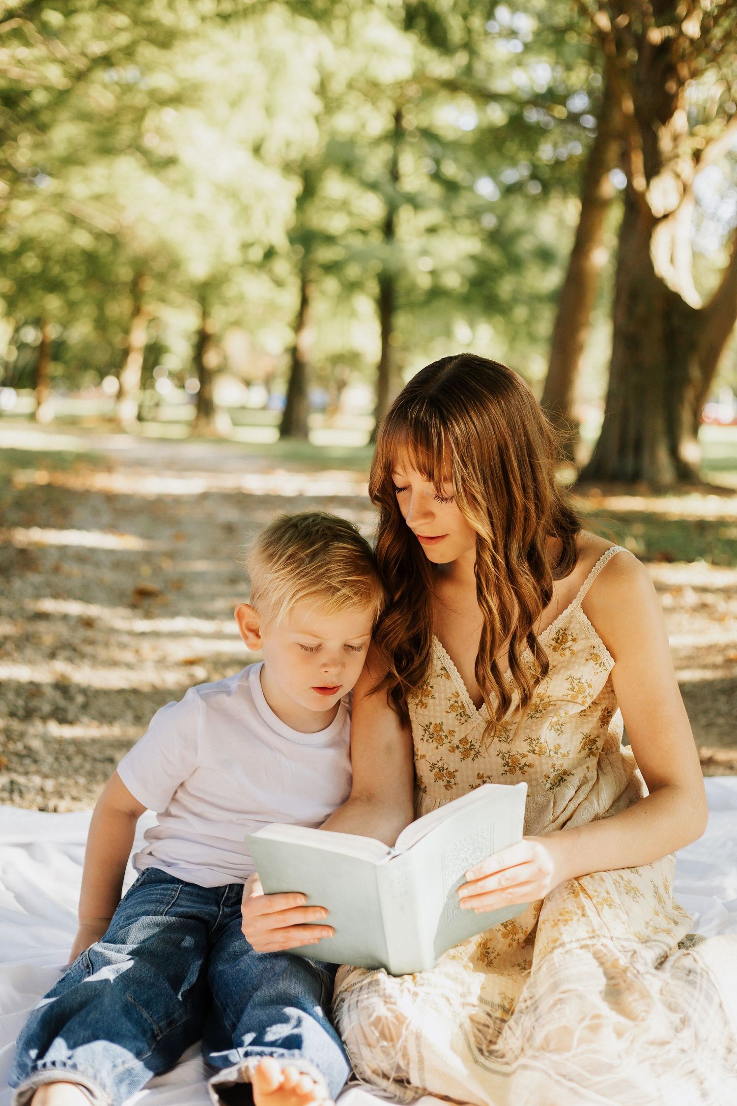Parent and child reading a book together in a sunny park setting.