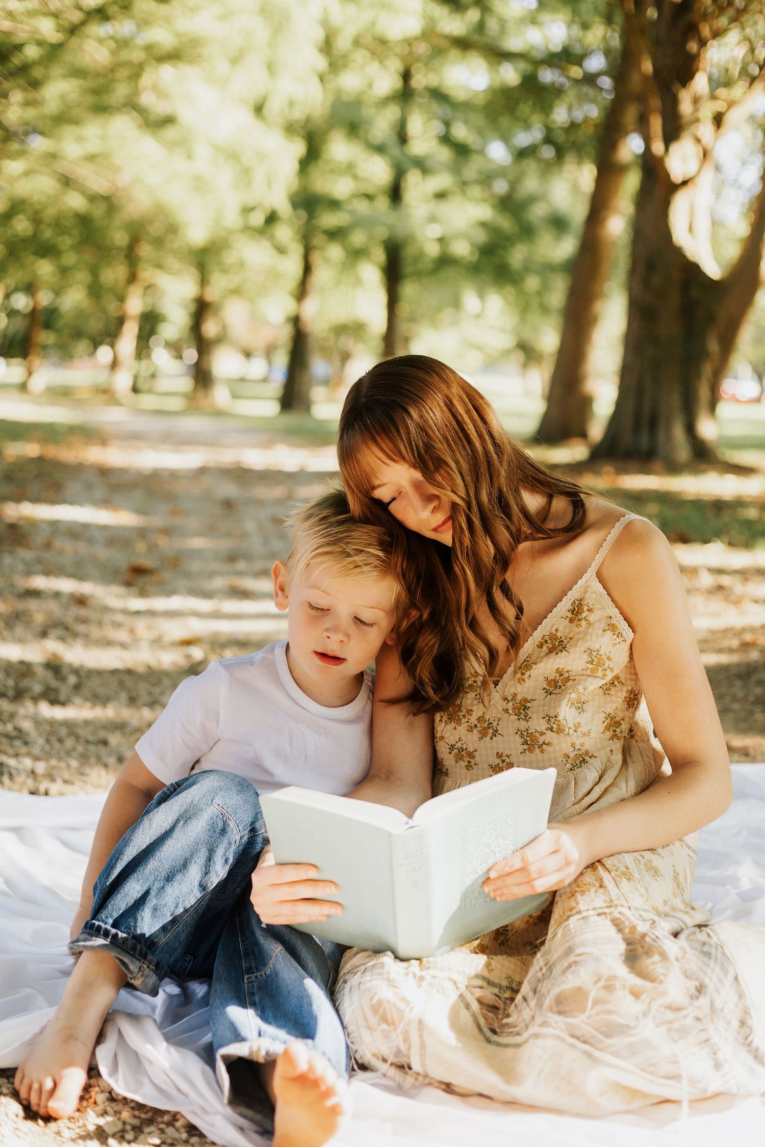 A tender reading moment shared on a blanket under sunlit trees in a park.