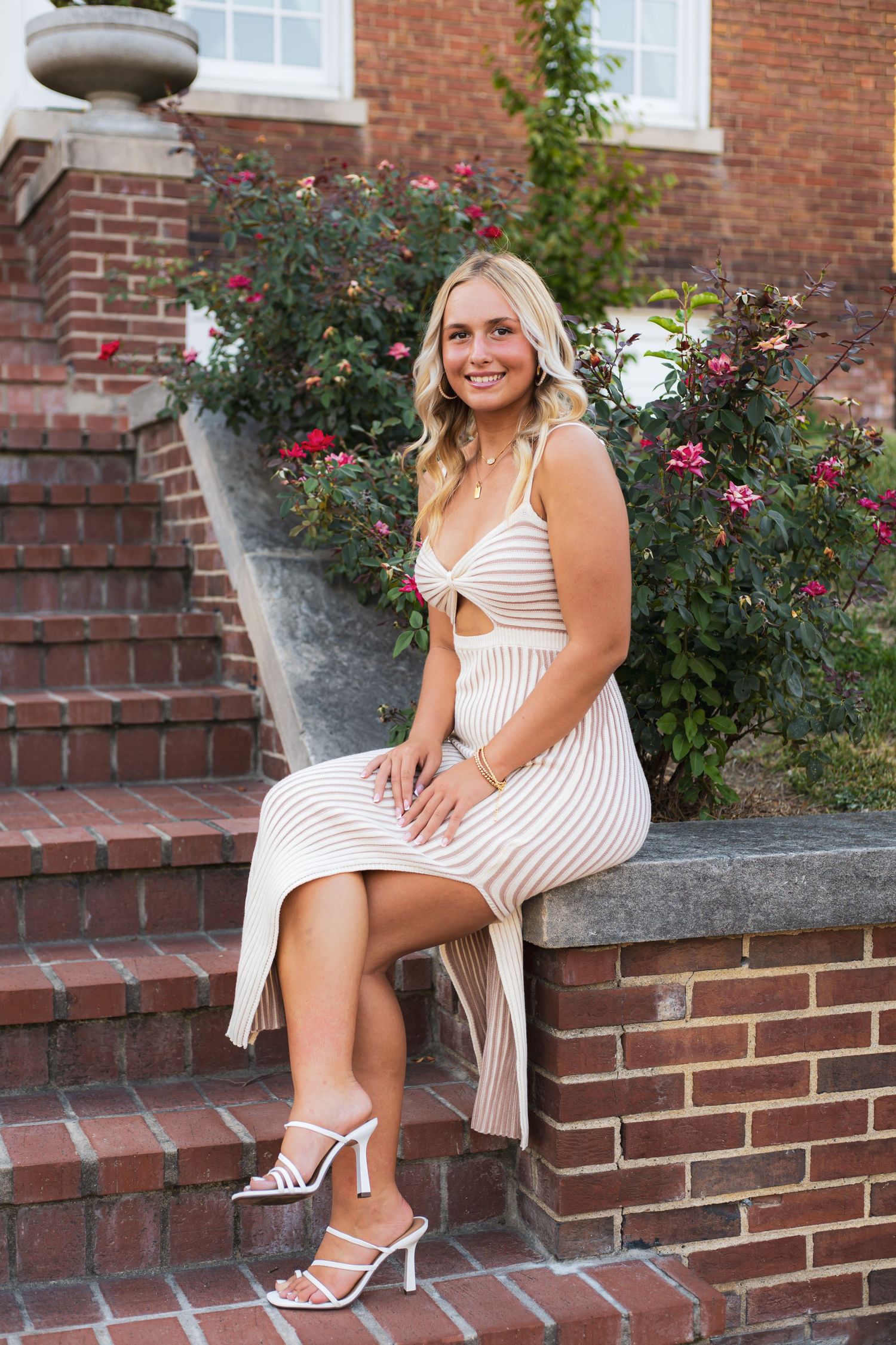 Woman in white dress seated on brick steps with blooming rose bushes.