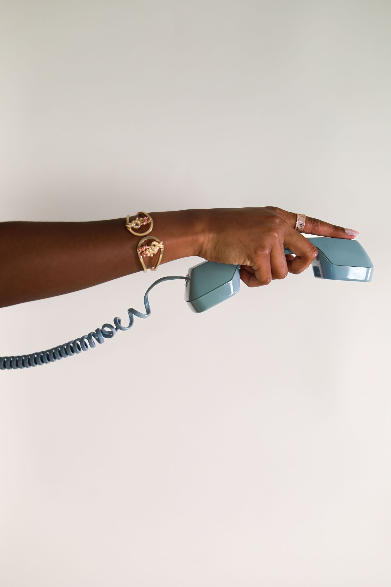 Hand holding blue vintage telephone handset with coiled cord on white background.