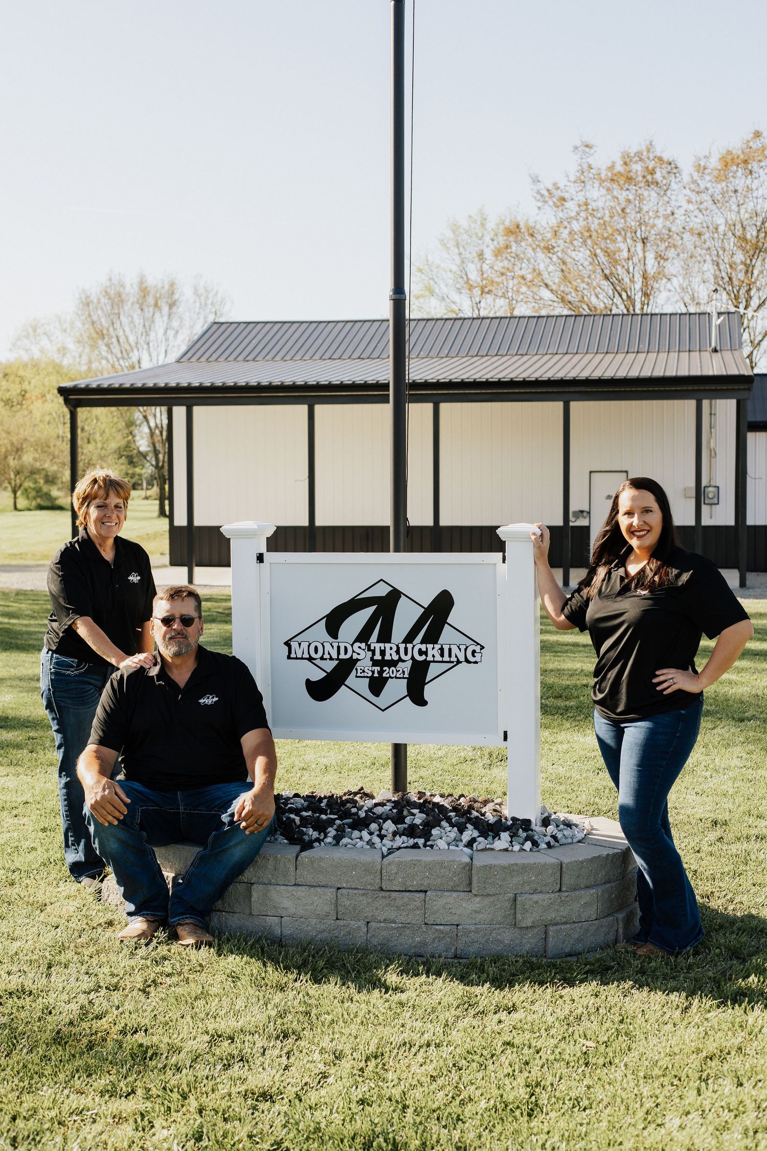 Group photo by a white stone business sign on grassy landscape.